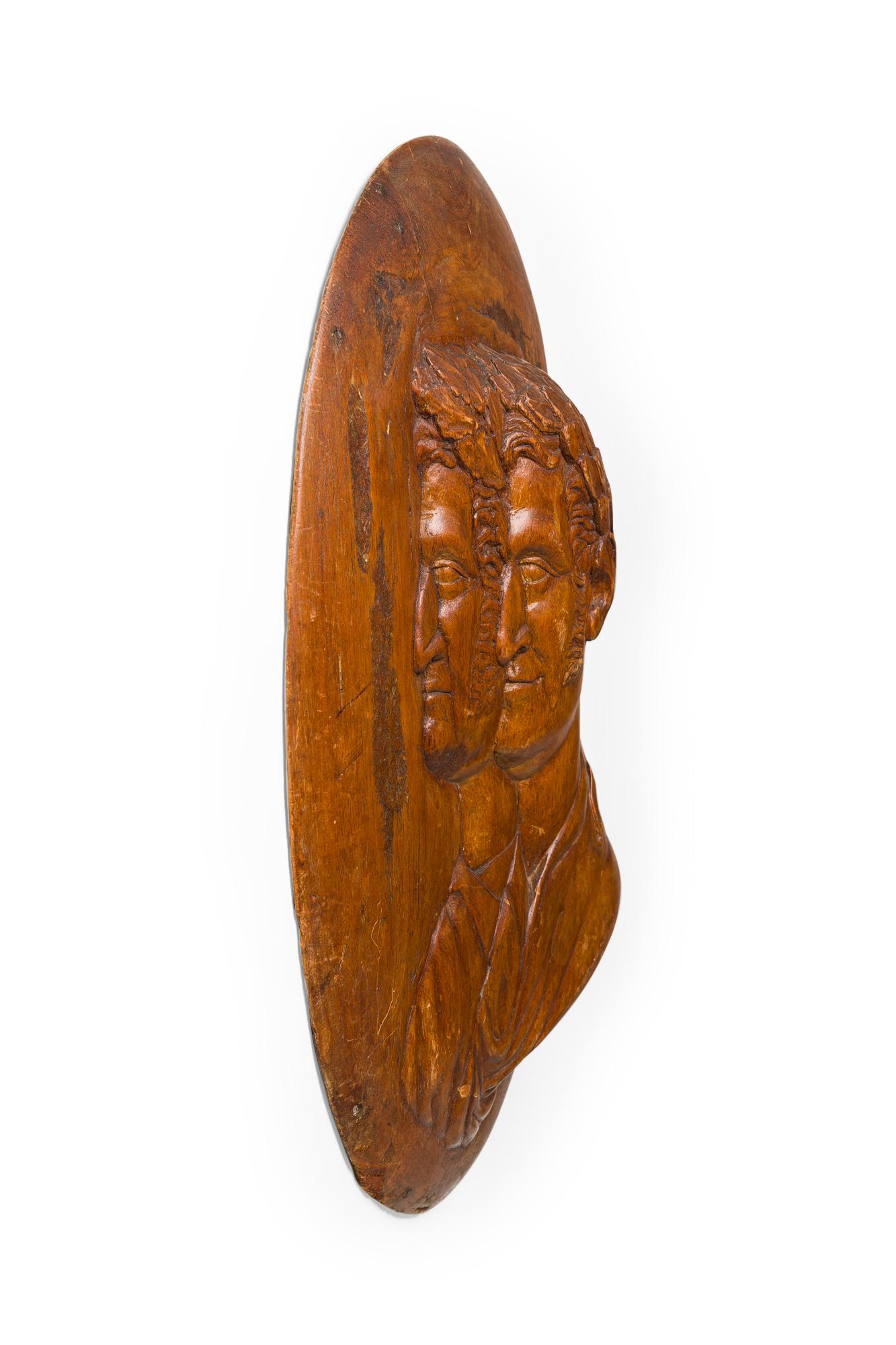 Ovale Wandtafel aus italienischem Nussbaumholz im neoklassizistischen Stil (19. Jahrhundert) mit 2 römischen Senatsköpfen in Relief.
 