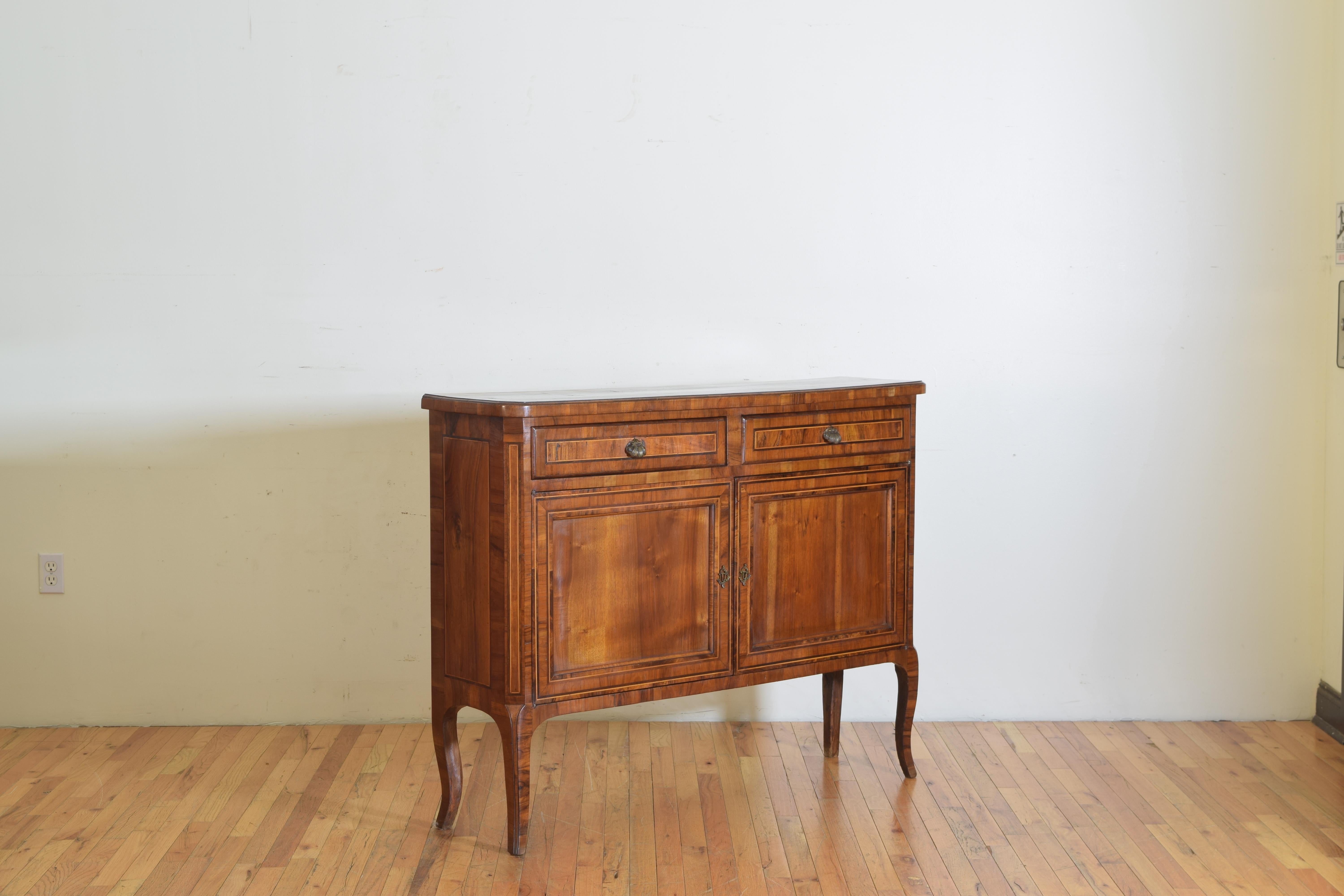 Having a rectangular top with rounded front edges above a conforming case housing two drawers over two doors, the credenza covered in walnut and mixed wood veneers, with bronze hardware, raised on flared legs.