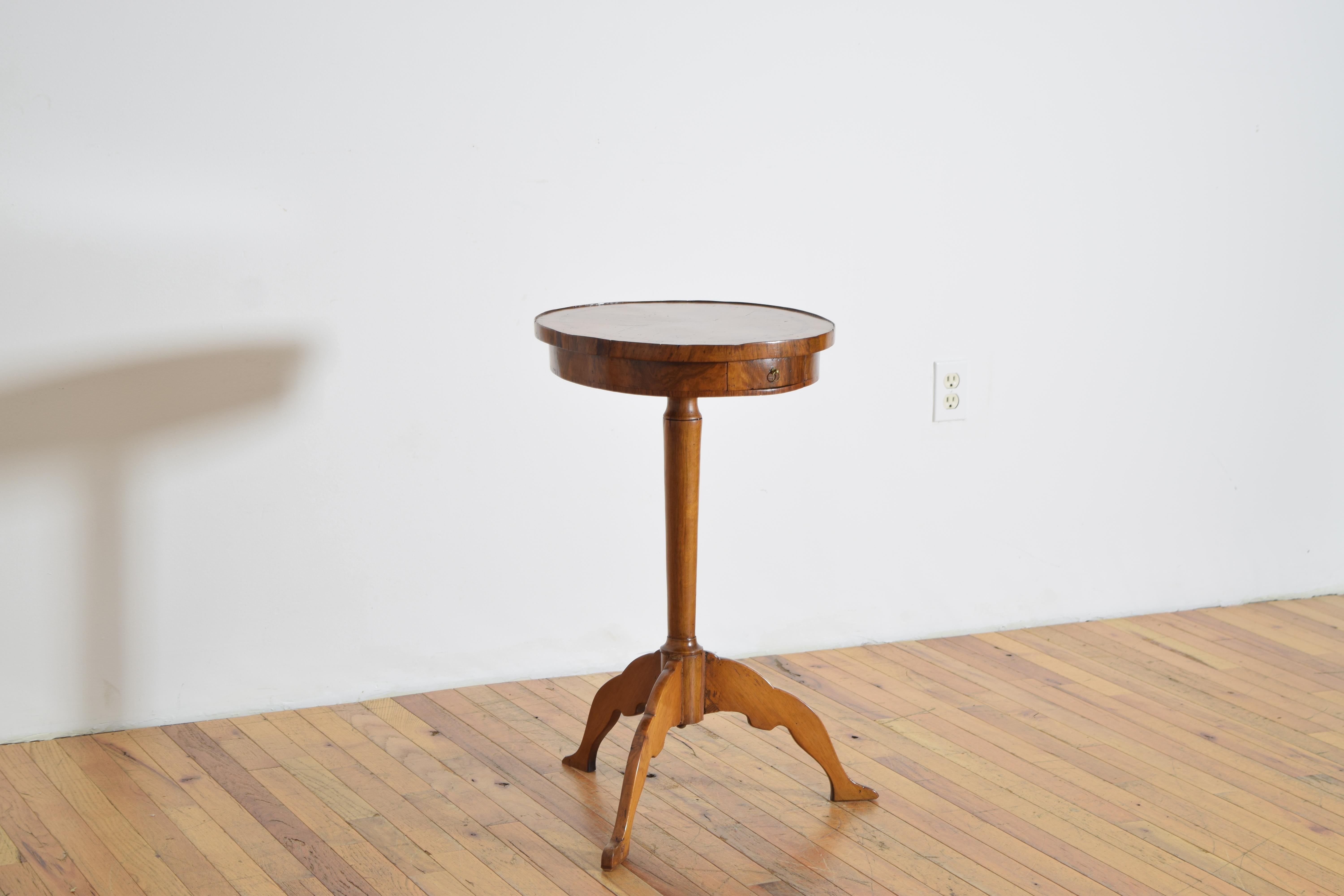 having a D-shaped oval top with a slightly raised gallery edge and a bookmatched veneered surface, the case housing one drawer and supported by a turned standard, the interestingly shaped legs ending in pad feet
