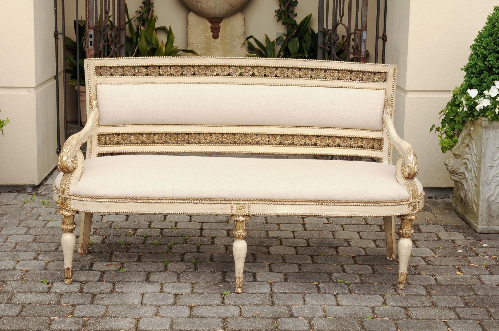 An Italian neoclassical period wooden settee from the early 19th century, with original paint, gilded accents, floral motifs and new upholstery. Born in Italy during the early years of the 19th century, this exquisite neoclassical settee features a