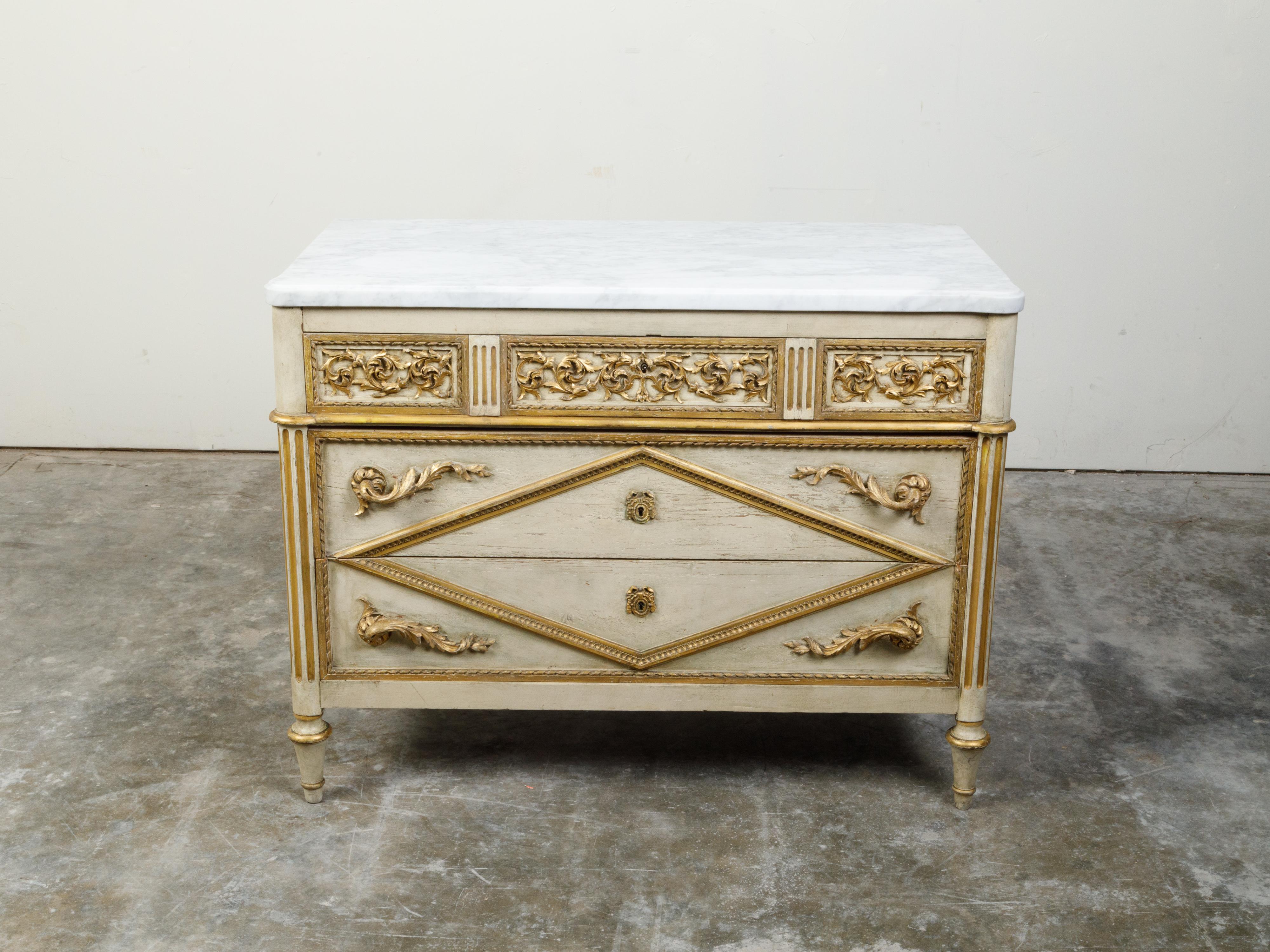 An Italian Neoclassical period painted three-drawer commode from the early 19th century, with marble top, gilt and carved motifs. Created in Italy during the early years of the 19th century, this Neoclassical commode features a rectangular white