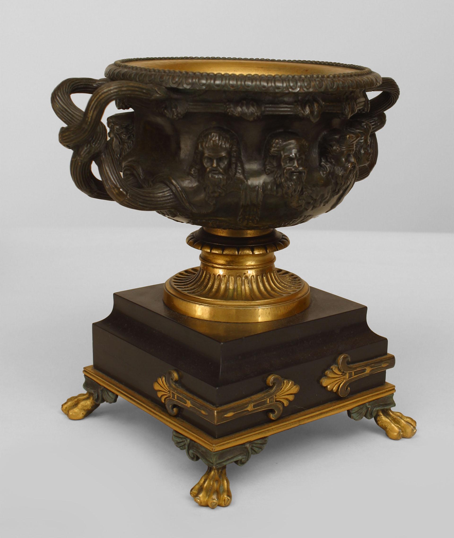 Pair of Italian neoclassical (19th century) bronze and gilt trimmed urns surrounded by Greek masks and having intertwined handles resting on a square black marble base over claw feet.