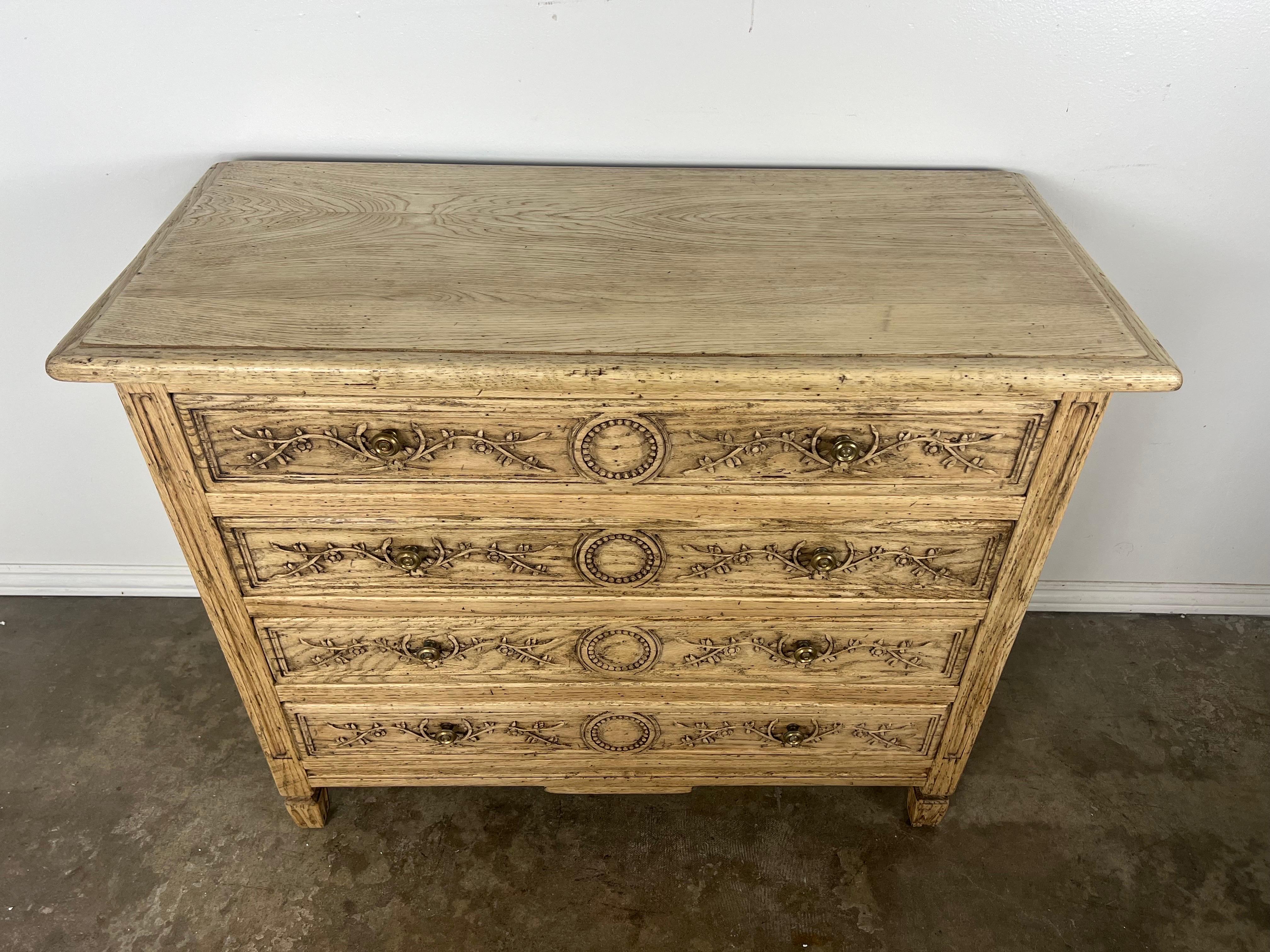 Mid 20th Century Neoclassical style chest of drawers.  The chest has four drawers for plenty of storage. The drawers are decorated with carved vines flanking a beaded circle.  Brass hardware.