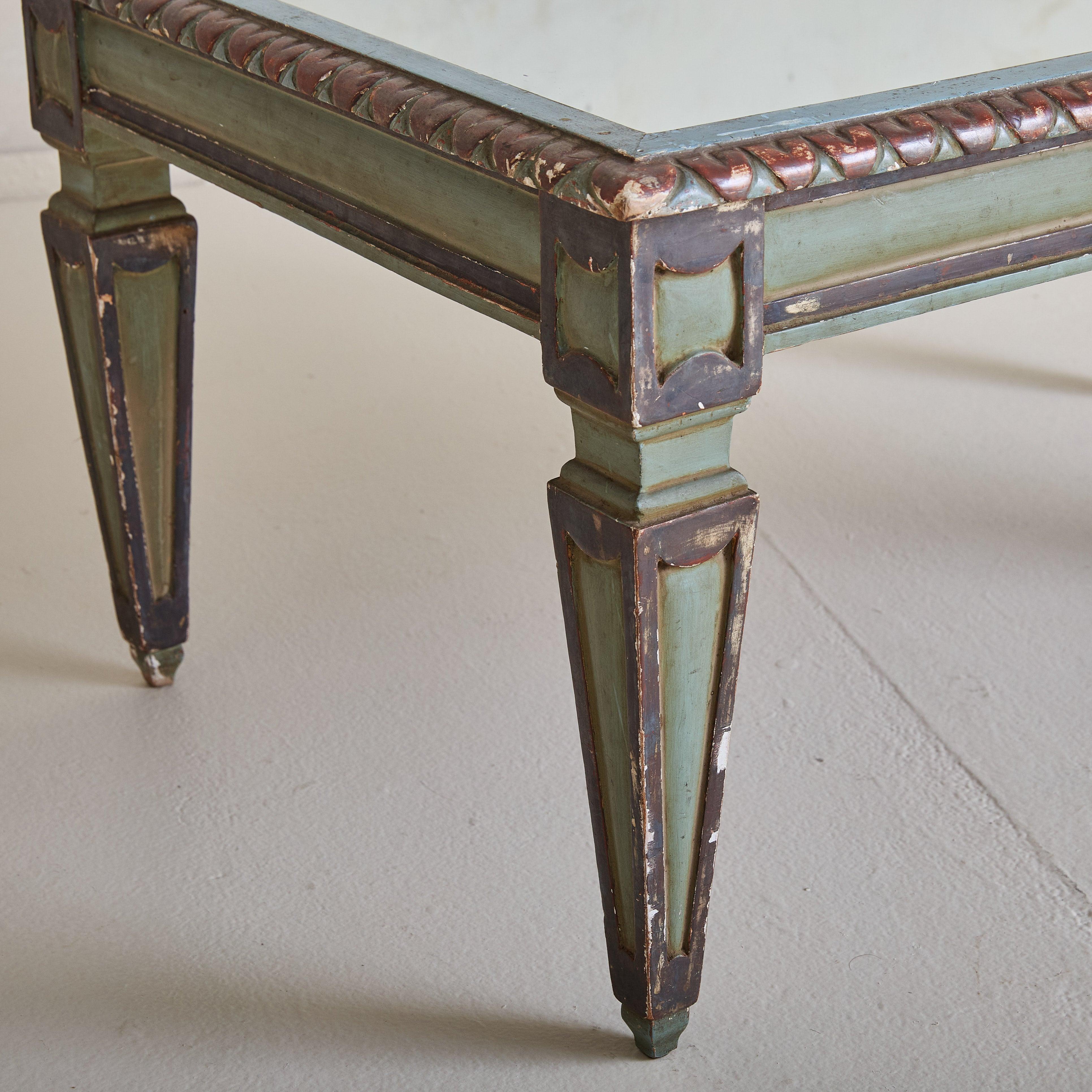 An antique Italian Neoclassical-style coffee table with fluted, column-like legs and distinctive medallion motifs. Crafted from solid wood, it features a soft cerulean painted finish accented with chocolate brown and rust red. The tabletop is inset