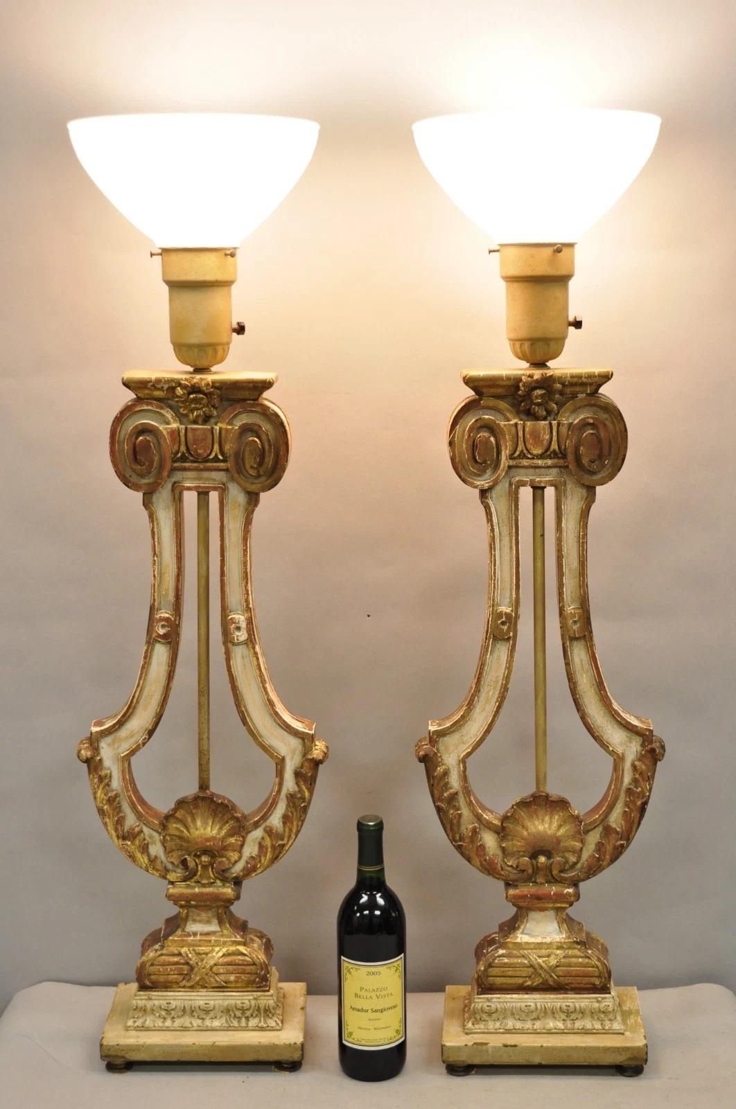 Impressive Vintage Italian Neoclassical Cream & Gold Gilt Distressed Finish Carved Wood Harp Column Table Lamps on Painted Metal Bases and Raised on Brass Feet - a Pair. Circa Early 20th Century. Measurements: 40