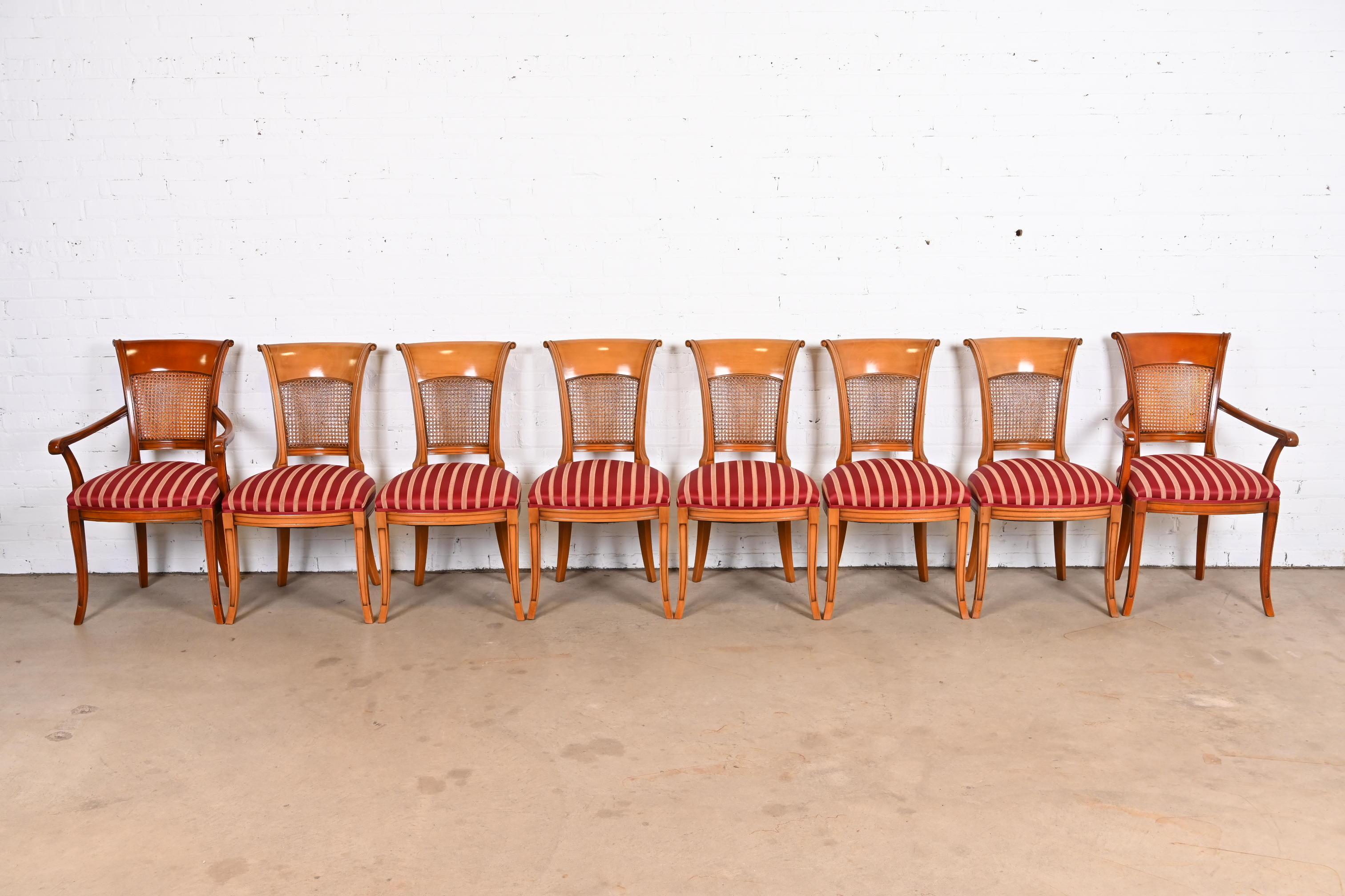 A gorgeous set of eight Neoclassical style dining chairs.

Italy, 20th century.

Solid carved fruitwood frames, with caned backs and striped satin upholstered seats.

Measures:
Side chairs - 19.25