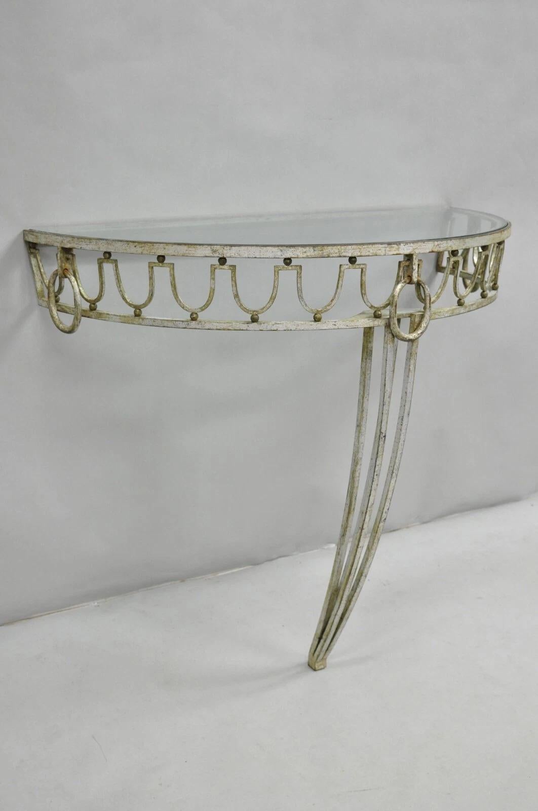 Consola italiana neoclásica de la época Hollywood Regency de hierro dorado con volutas. El artículo presenta una elegante forma Art Decó, un acabado dorado plateado envejecido, una tapa semicircular de cristal demiluna y artesanía italiana de