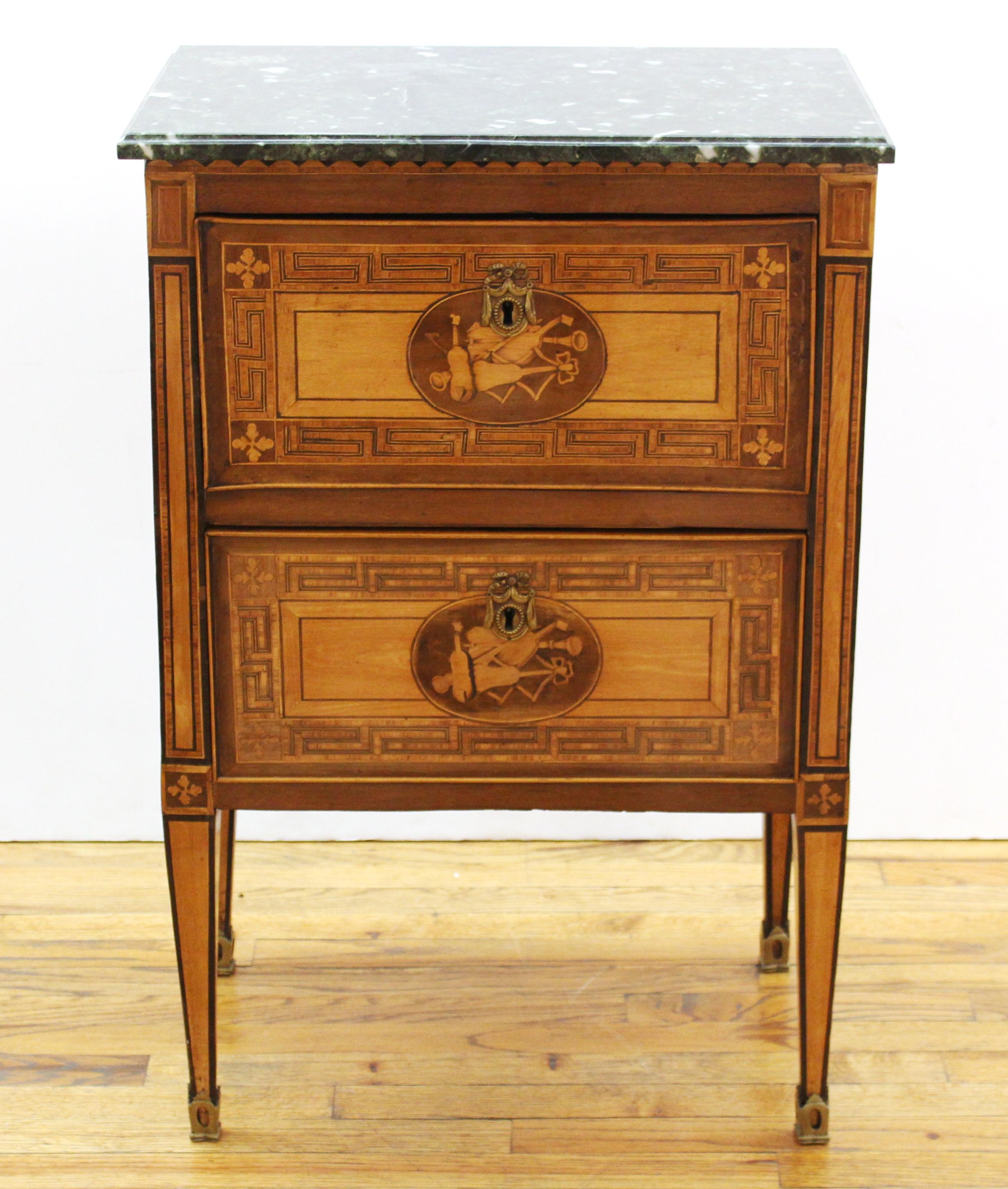 Italian Neoclassical inlaid commodino, circa 1800, the verde antico marble top above the marquetry and parquetry inlaid case, the two drawers centered with cartouches of a musical trophy, raised on tapered square legs. Measures: 34