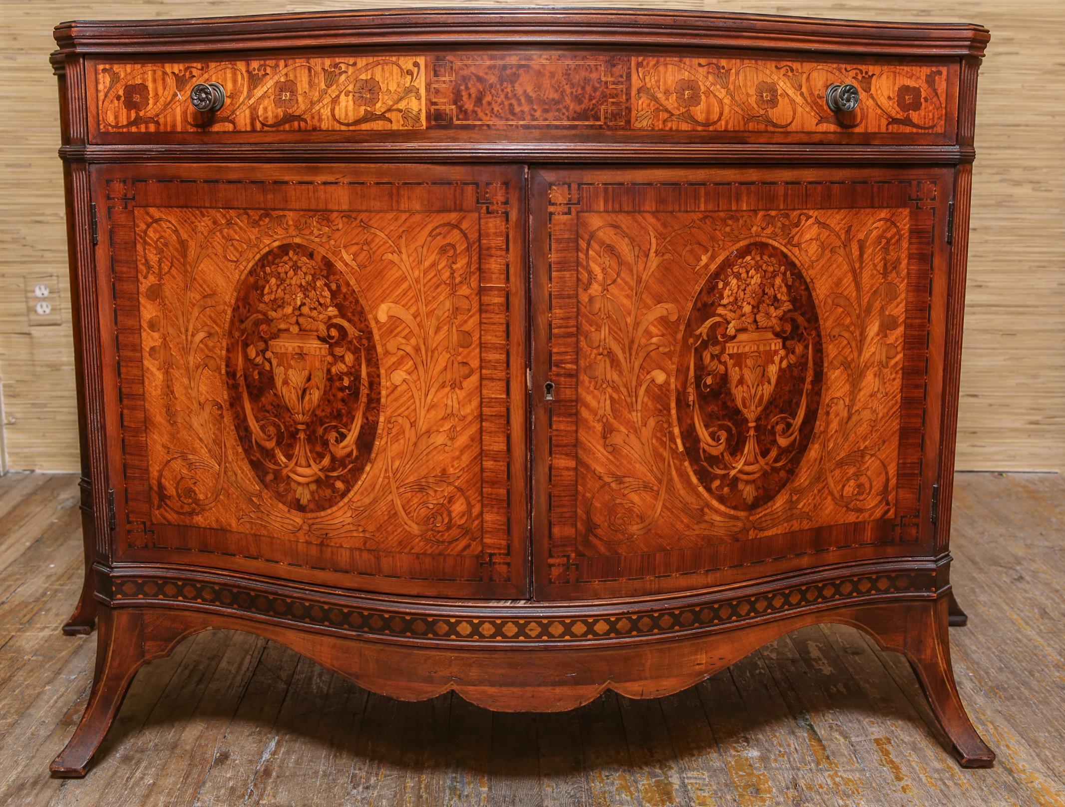 Italian neoclassical Revival manner serpentine-shaped commode or cabinet in mahogany with extensive fruit-wood marquetry. The central compartment doors with medallions contain three drawers with gilt pulls with turquoise embellishments. In good