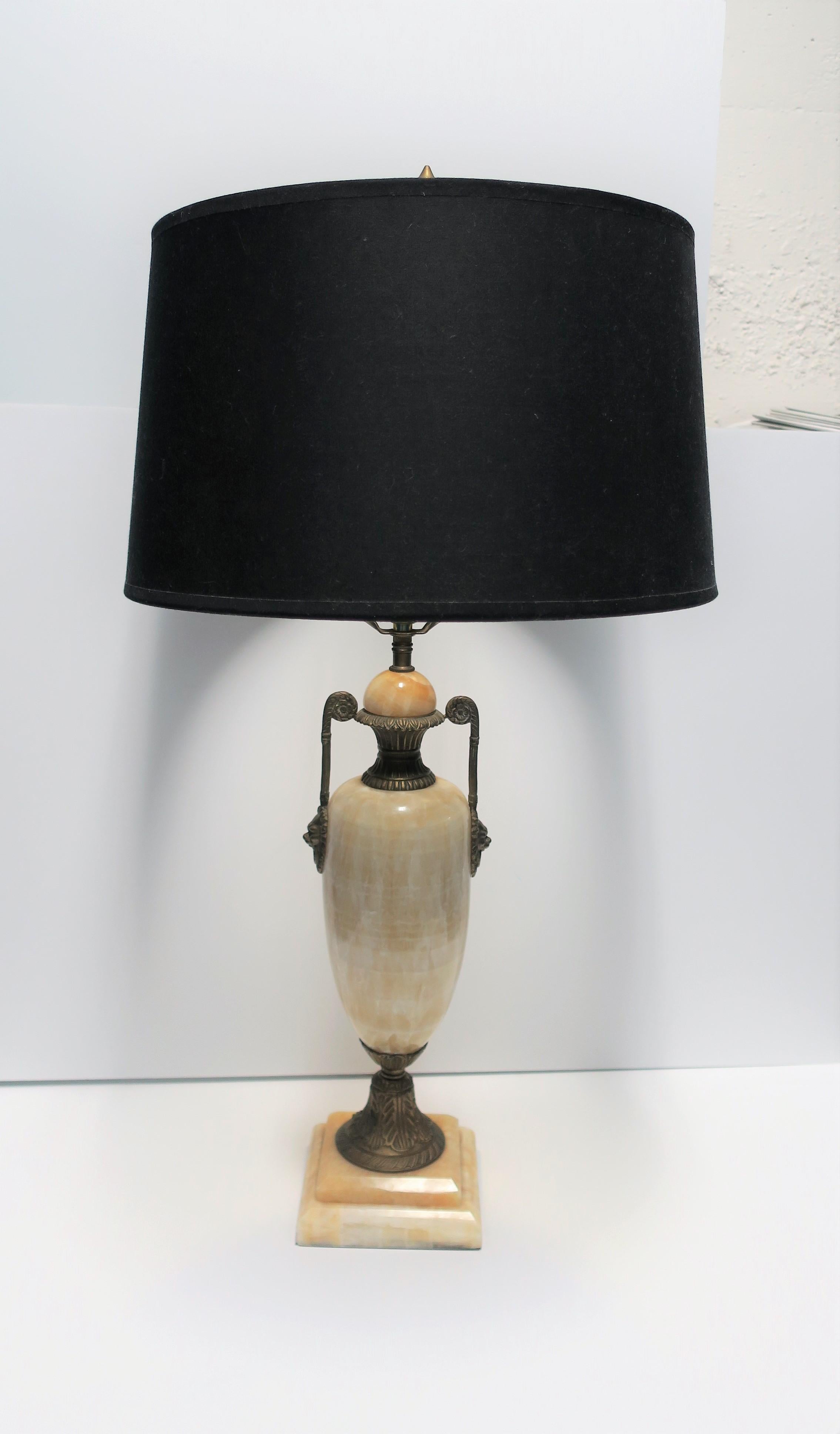 A substantial solid beige or sand colored onyx marble and brass urn form desk or table lamp with lion-head detail in the Regency style, circa late-20th century. Lamp includes original brass finial. 

Measurements:
Base: 5.5