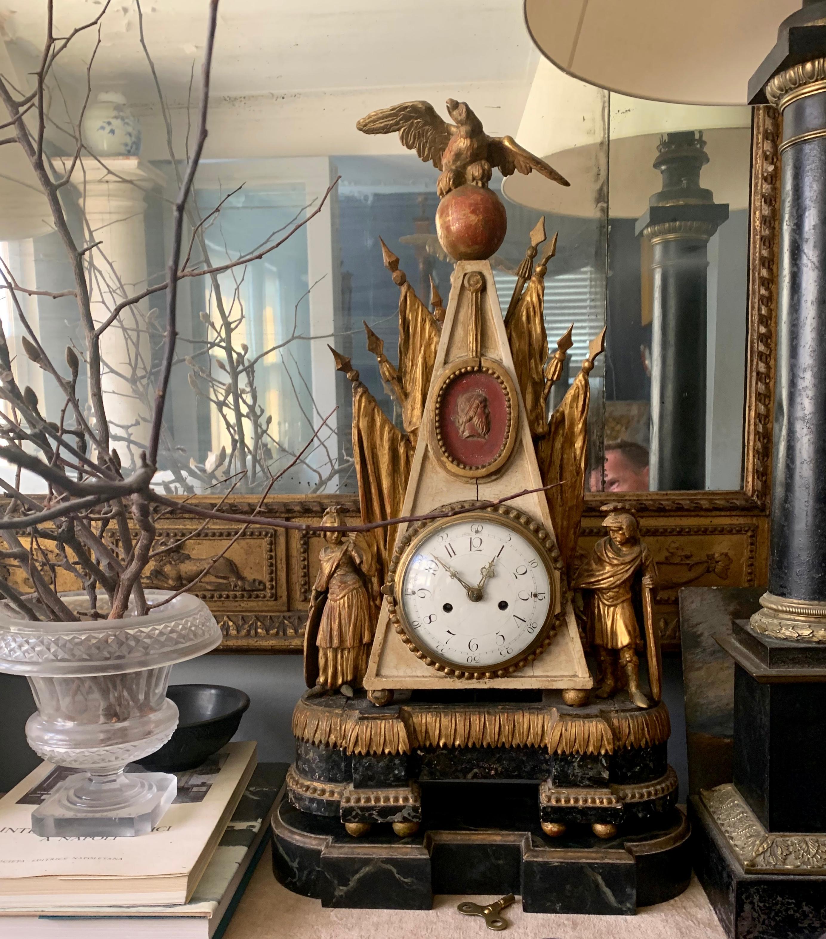 Horloge italienne néoclassique en bois doré. Pendule de cheminée de l'époque de l'Empire romain militaire, en forme d'obélisque surmonté d'un aigle extraordinaire aux ailes déployées sur un orbe rouge, au-dessus de drapeaux sculptés en doré flanqués