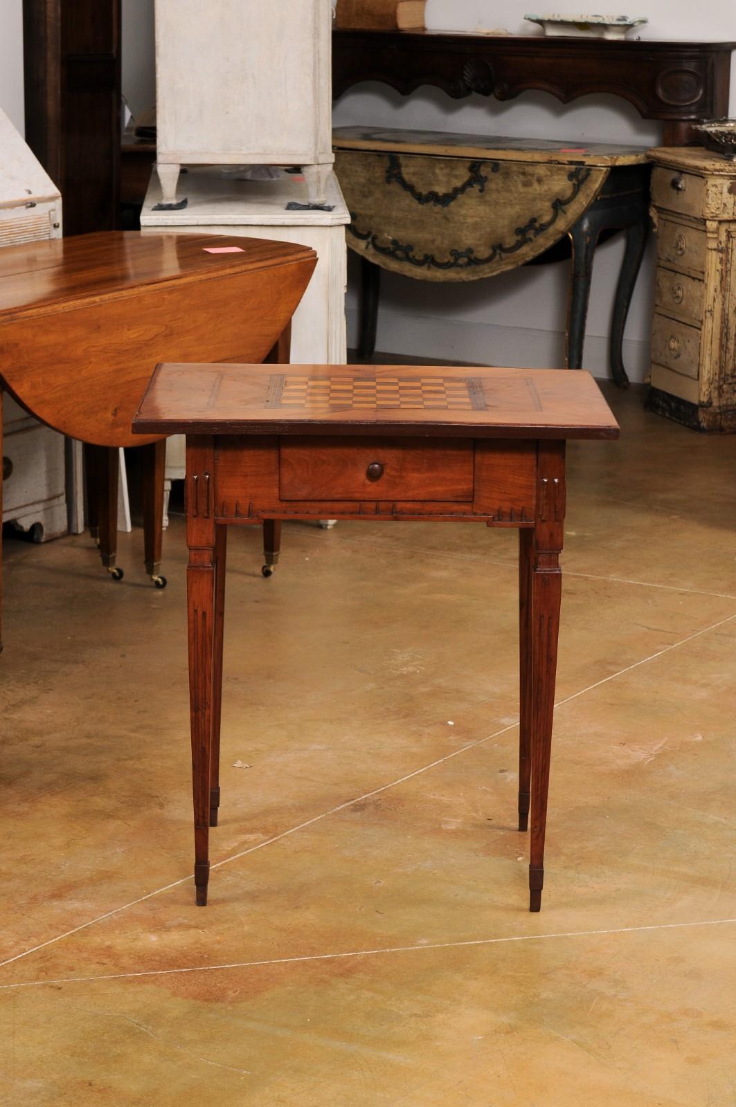 An Italian Neoclassical period walnut and mahogany game table from the 18th century, with checkerboard marquetry décor, single drawer and fluted tapering legs. Created in Italy during the 18th century, this Neoclassical game table features a