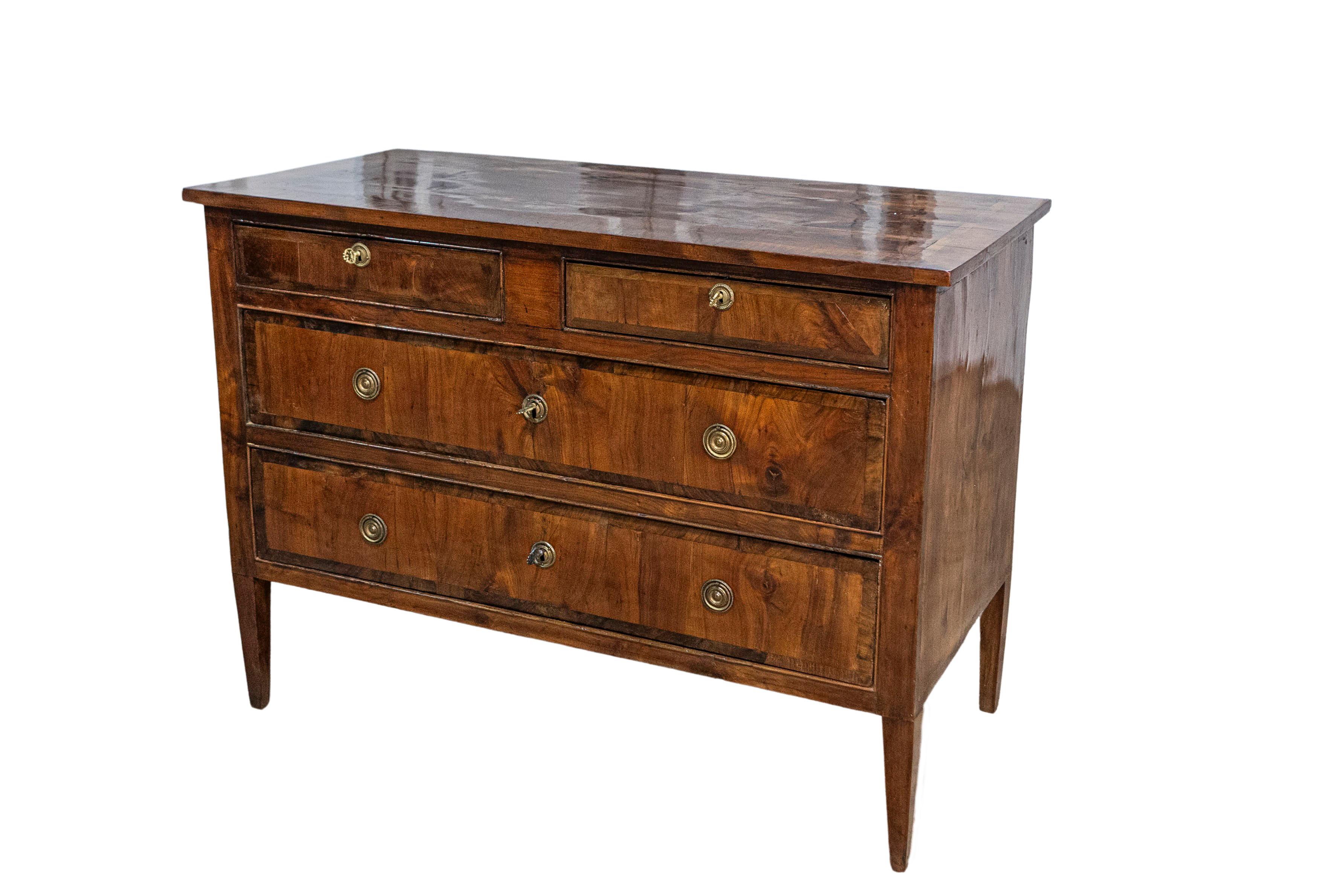 An Italian Neoclassical walnut commode from the 18th century with four drawers, cross-banding and tapered legs. This Italian walnut commode, dating back to the 18th century, presents a timeless elegance with its classic structure and fine details.