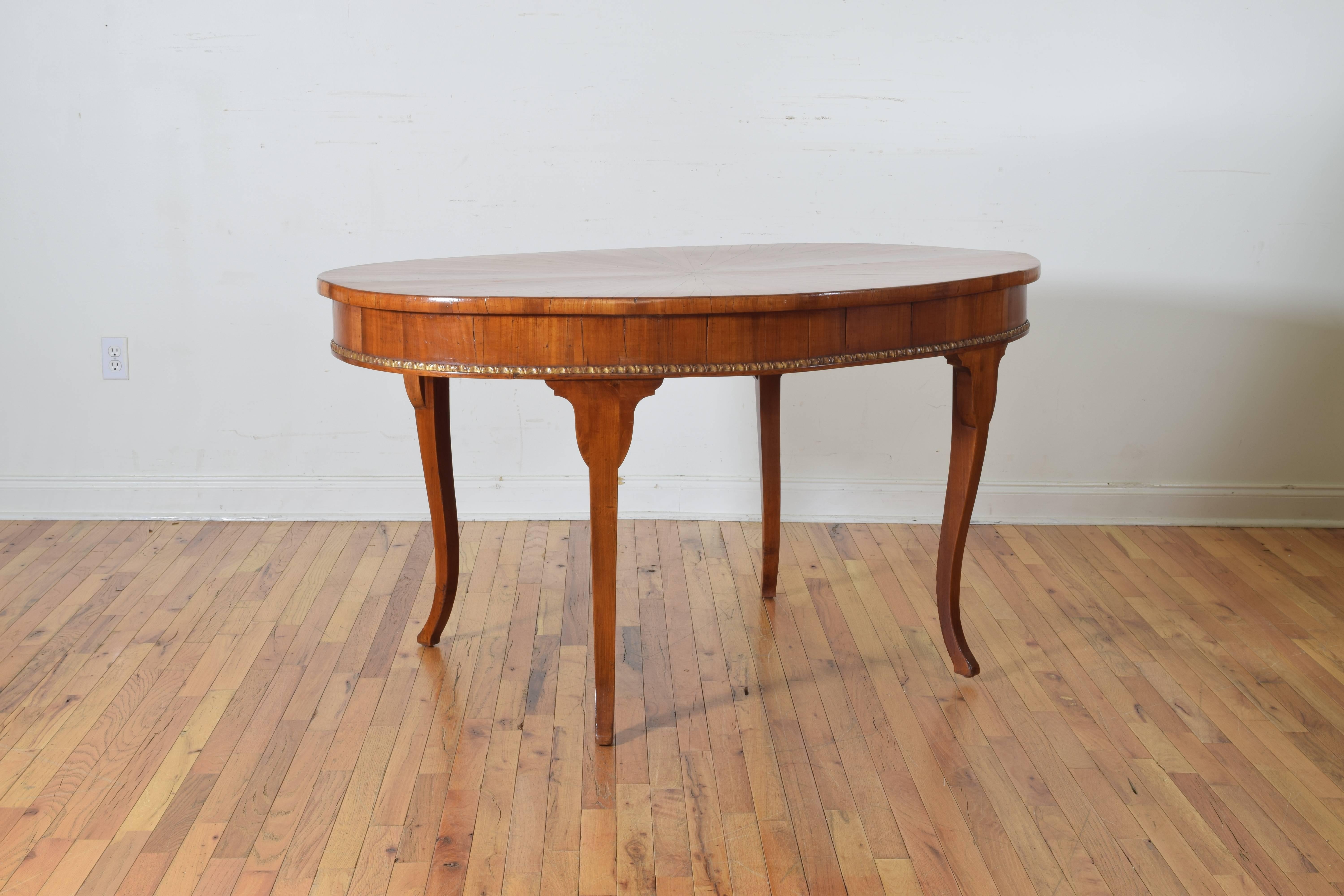 The oval top with radial veneers, the deep apron with a carved and gilded bottom molding, raised on interestingly shaped curving legs.