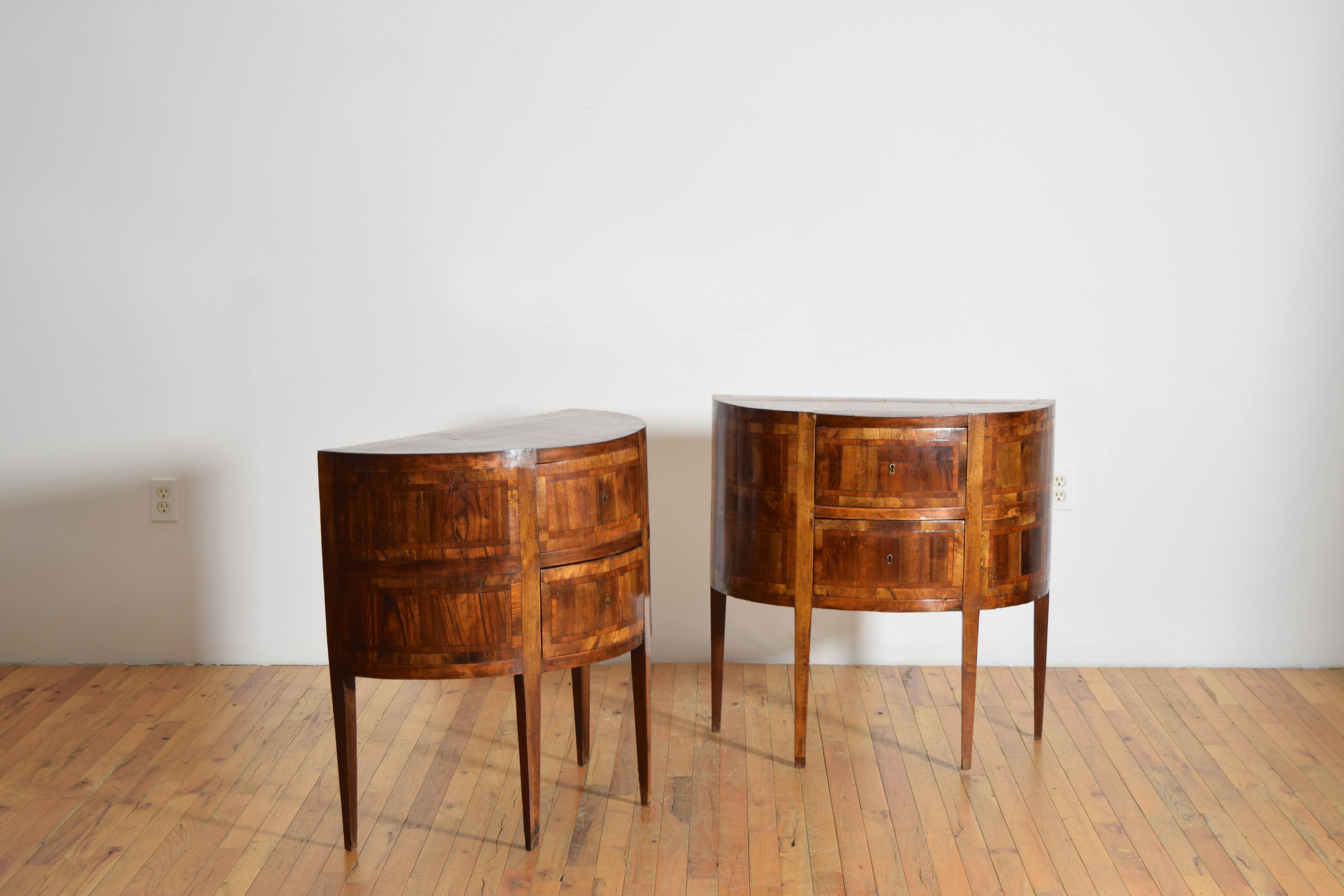 each commode of half-round form and having extensive patterned walnut inlays, two drawers, raised on square tapering legs
