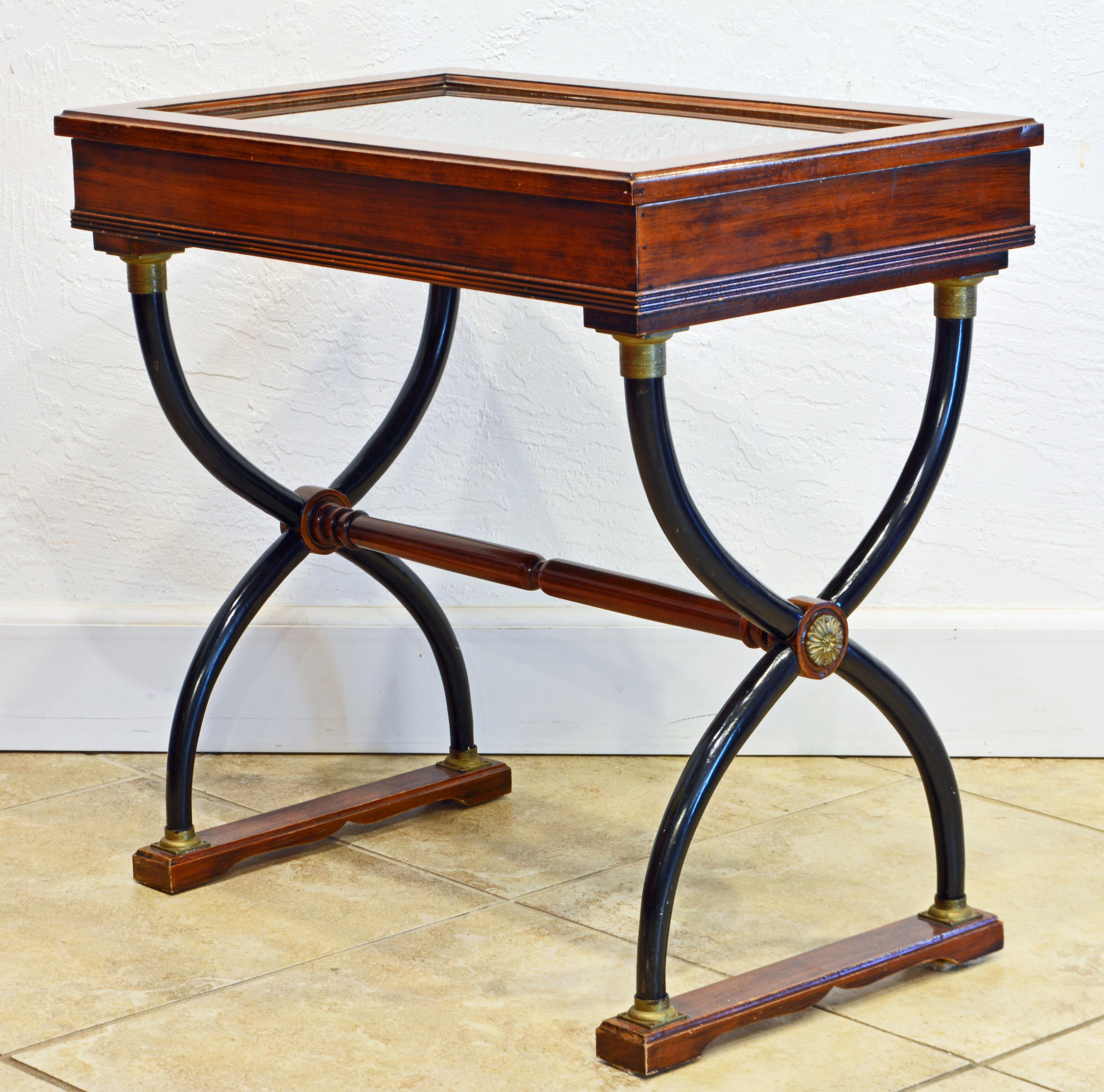 Resting on double sets of curule style ebonized and bronze mounted legs joined by a turned stretcher with bronze rosettes this walnut vitrine table features a glazed top opening up to the display interior. Early 20th century.