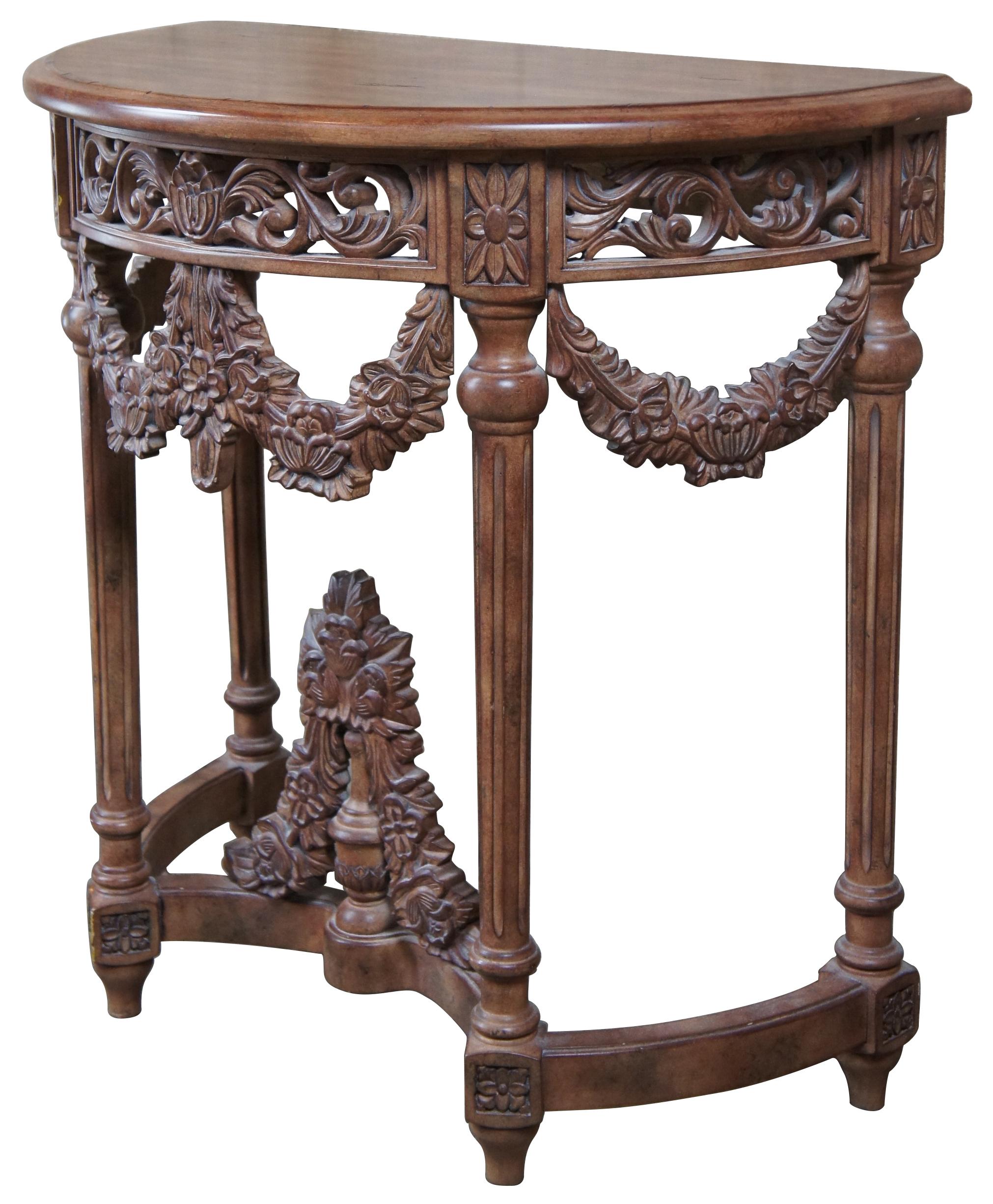20th century neoclassical Revival console or hall table. Features a demilune shape with a distressed walnut finish. Ornately designed with a pierced apron and floral drapery between fluted columns leading to a trestle style base with trophy finial