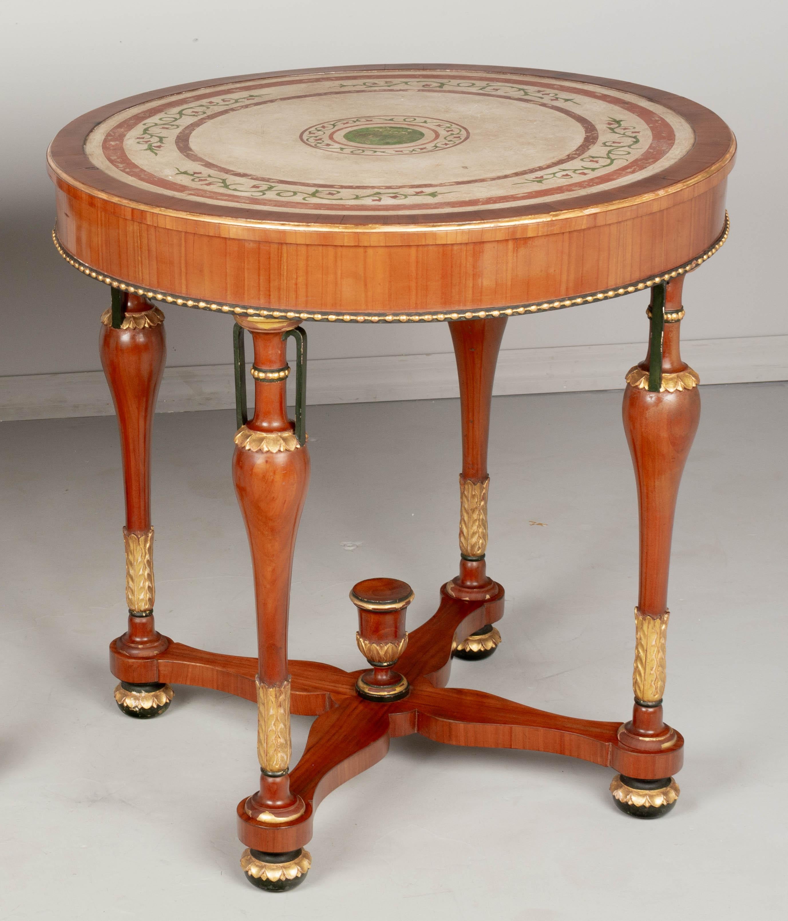 An Italian Neoclassical circular center table made of solid and veneer of cherry. The top is scagliola, a hand-painted plaster technique that resembles inlays in marble. Elegant turned legs with urn forms and gilded foliate decoration with bead