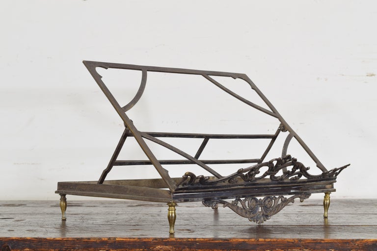 The open backrest adjustable and resting atop a rectangular frame raised on turned brass feet, the front sections with decorative leafage scrollwork, height is when fully extended in top position, first half of the 19th century.