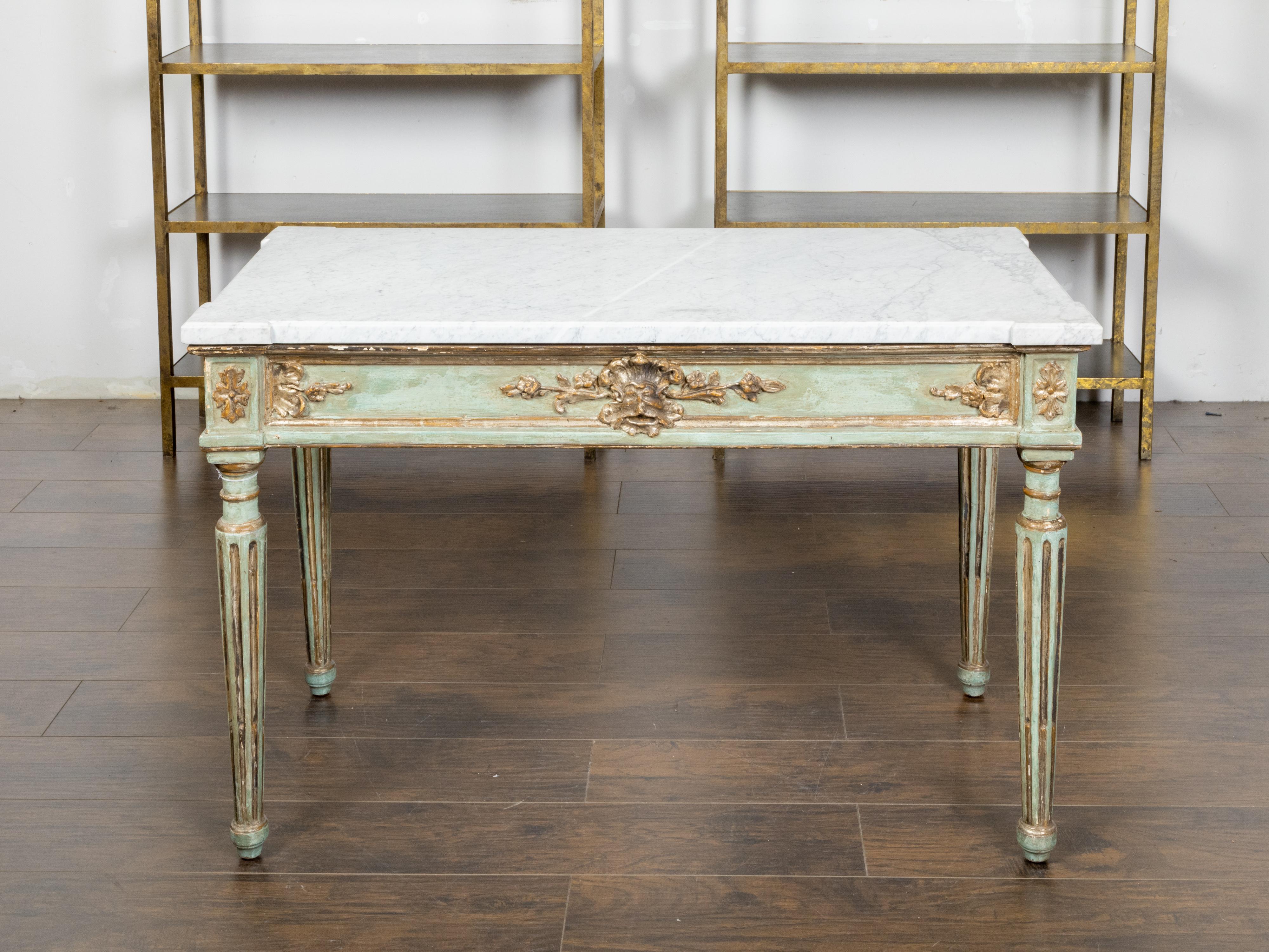 Table console en bois peint de style néoclassique italien du XIXe siècle, avec un plateau en marbre blanc, des feuillages, des coquilles et des visages de mascarons dorés et sculptés, et des pieds cannelés. Créée en Italie au XIXe siècle, cette