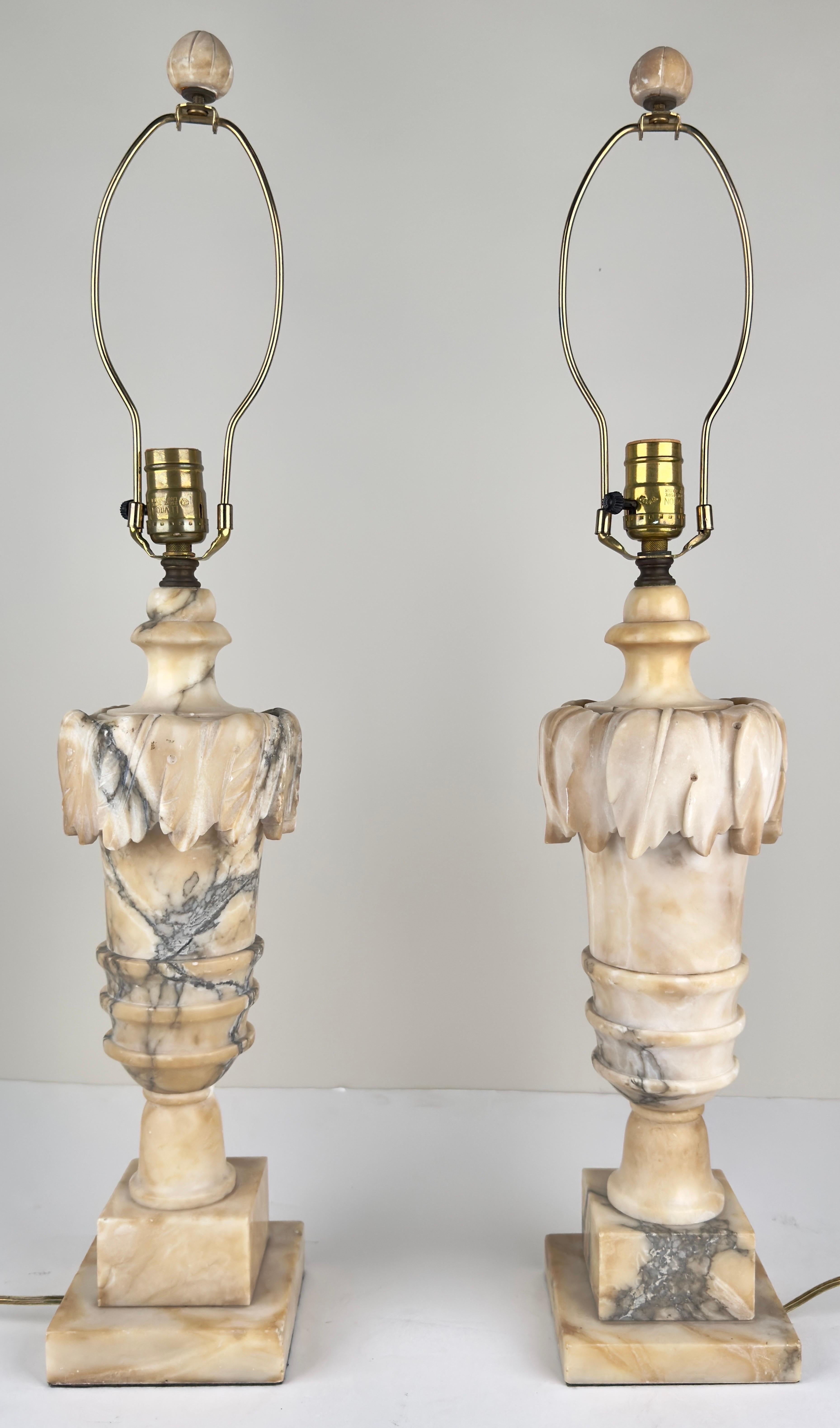 An elegant pair of Italian Neoclassical lamps crafted from Carrara alabaster. These lamps capture the essence of refined Italian craftsmanship. The lamps are designed in the form of stylized urns, a hallmark of neoclassical aesthetics, reminiscent