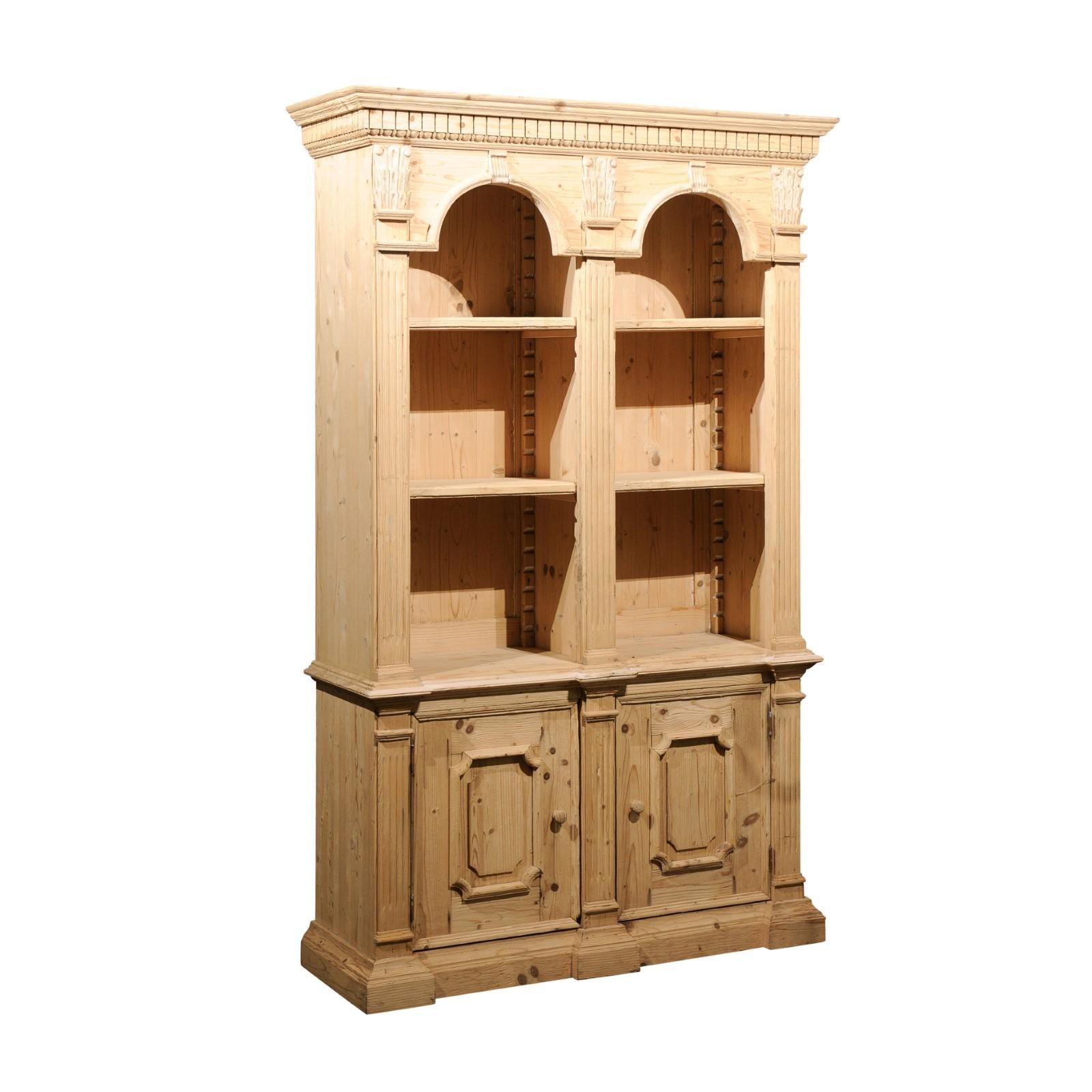 An Italian Turn of the Century Neoclassical style pine bookcase from the early 20th century with arched motifs, carved dentil, Corinthian and Doric capitals, fluted pilasters and molded doors. Created in Italy during the early years of the 20th