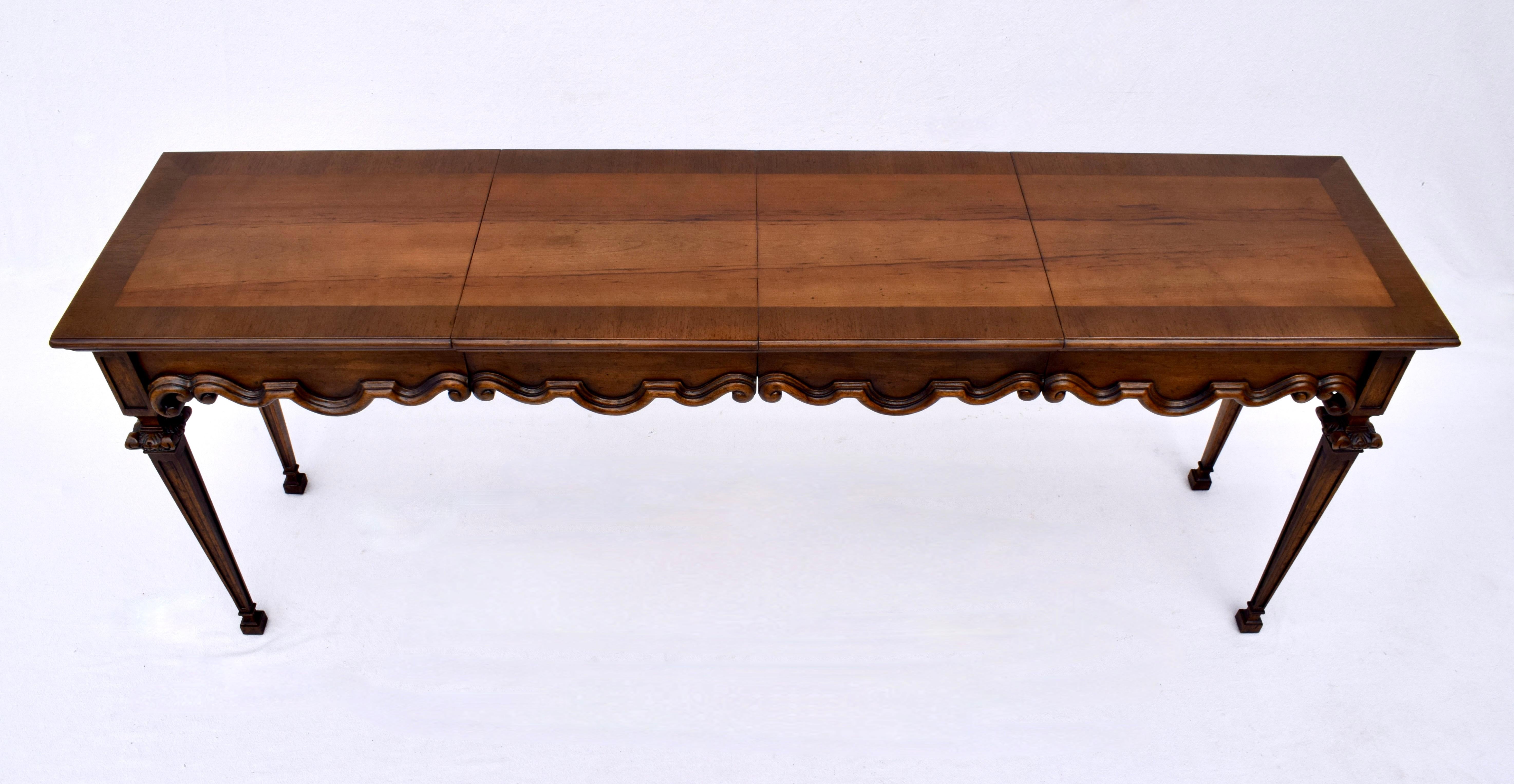 An unusual console table in the Neoclassical style with distinct Florentine design elements in the scalloped apron with bell flowers on the corner posts above square caps, ending in tapered legs. The versatile extendable two leaf top is newly