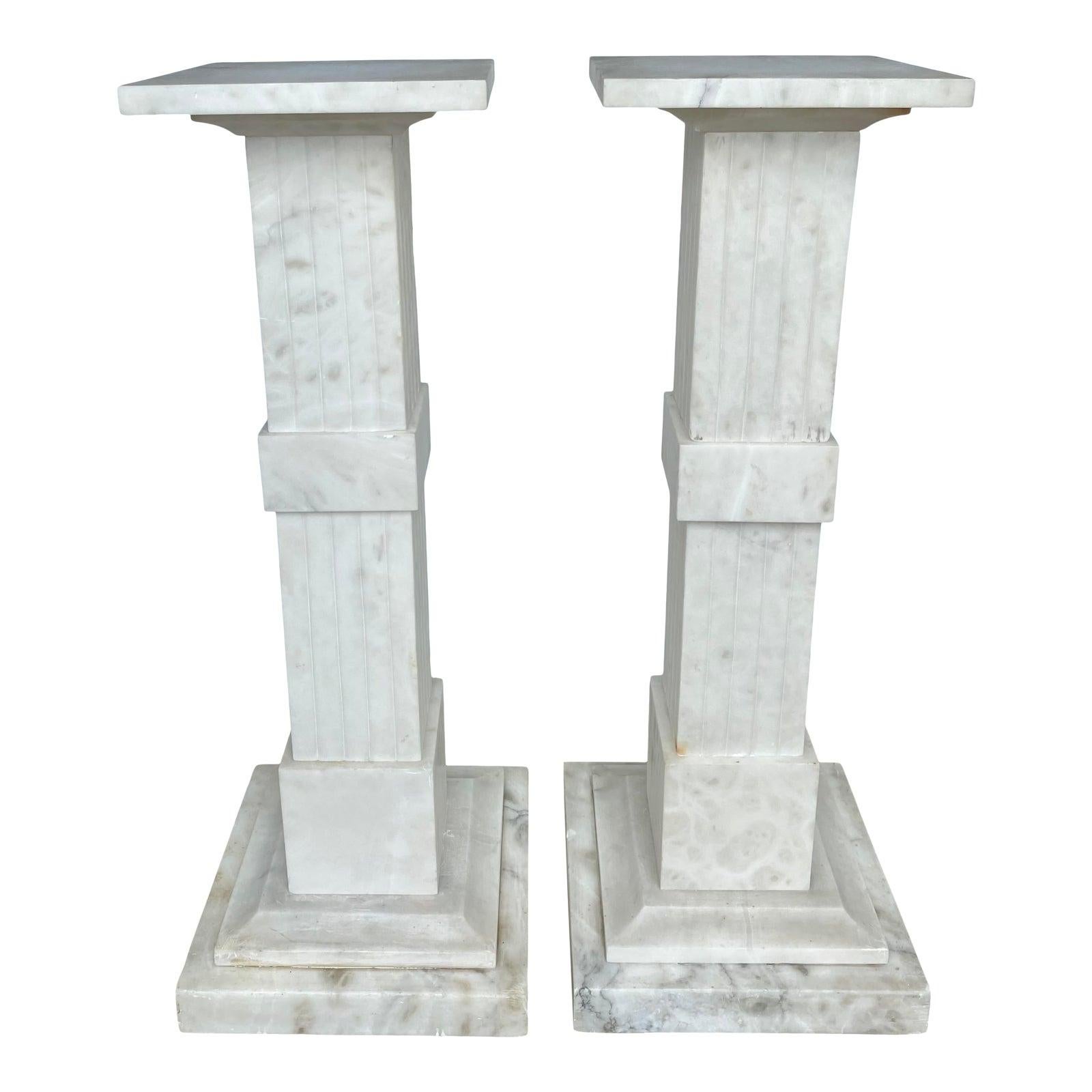 Impressive pair of neoclassical style white veined onyx stone pedestal columns. These large square columnar marble sculpture or plant stands feature square columns with fluted and band details atop stacked plinth bases. Each column is constructed of