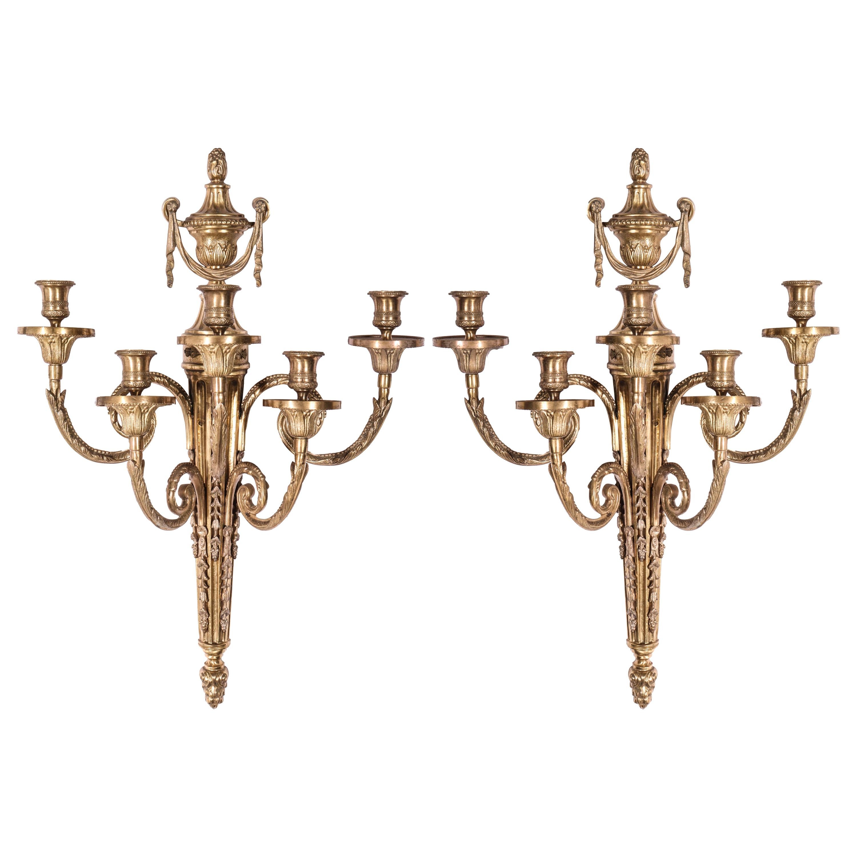 Italian neoclassical style pair of gilt bronze sconces with five branches. The pair is decorated with a flame finial topped acanthus wrapped urn, tassels and fluting. Marked with made in Italy tag on the back. In great vintage condition with