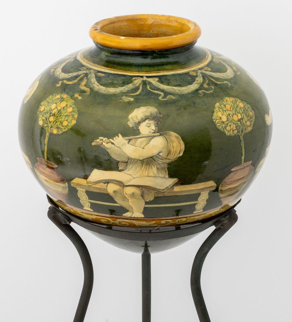 Vaso in ceramica smaltata in stile neoclassico italiano, raffigurante figure classiche che suonano strumenti su fondo verde con rifiniture in tan, montato su un supporto a treppiede in ottone patinato con tre piedi a zampa. 33