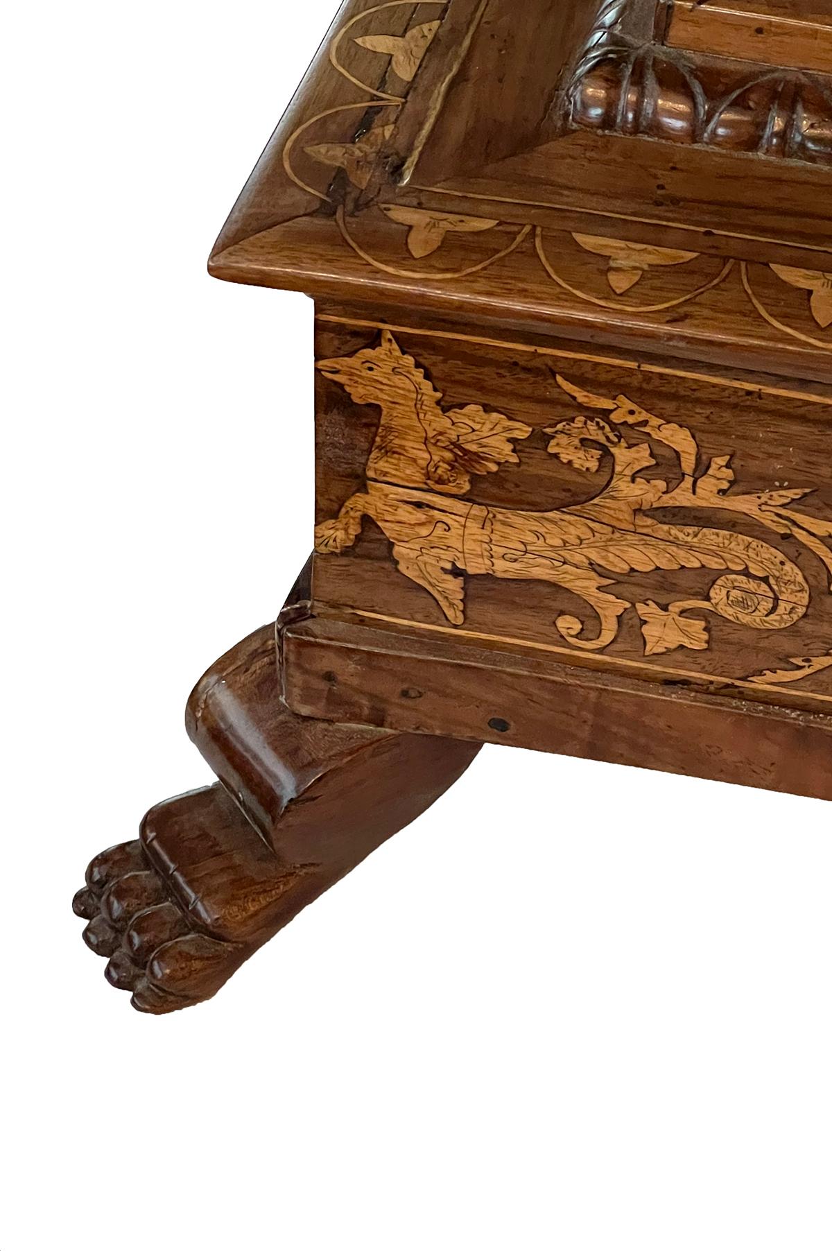 The round top with inlaid perimeter band depicting hunters and various animals amid a meandering foliate vine; raised on a splayed support over a square plinth with similar inlay; resting on four paw feet.