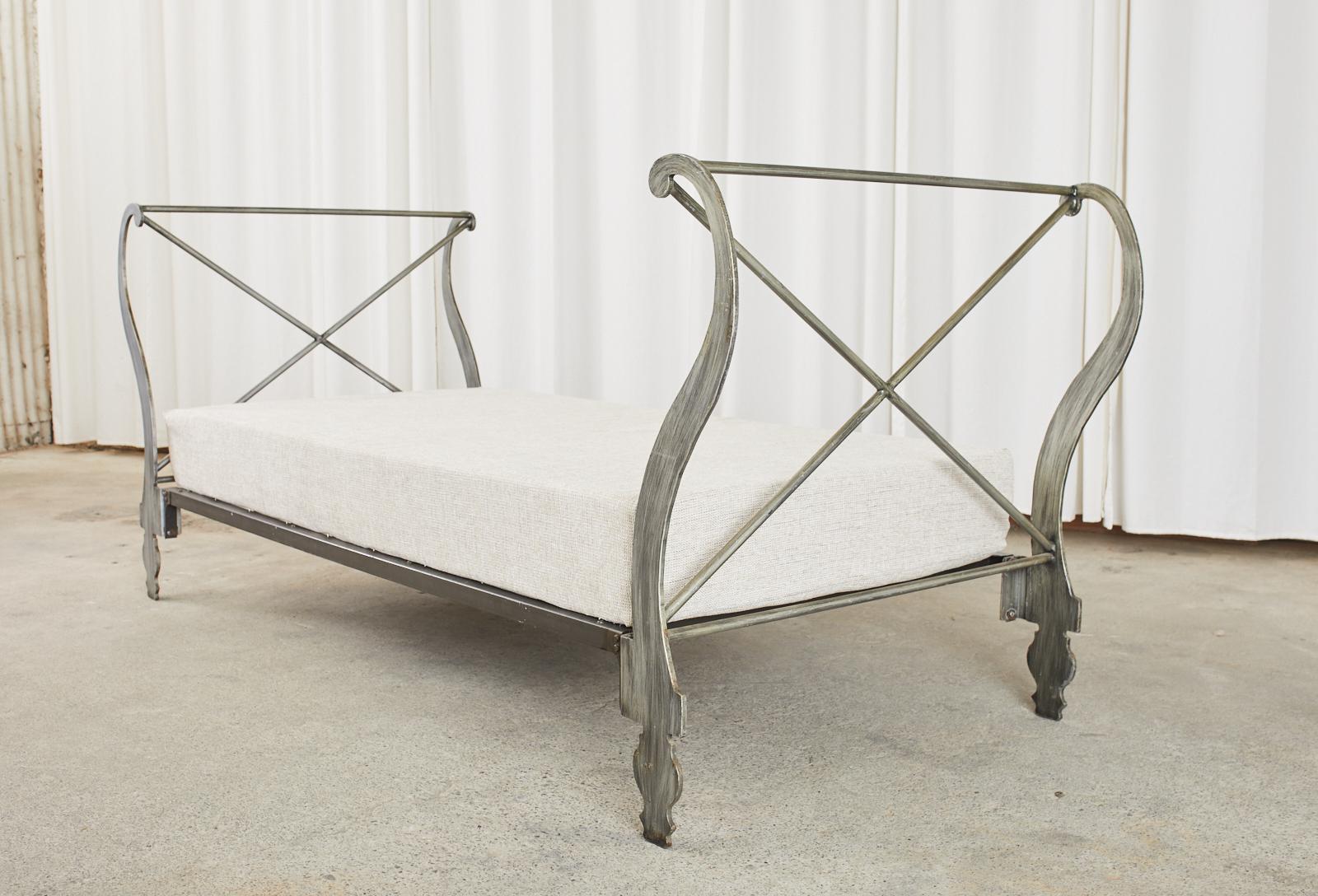Stylish Italian iron daybed featuring large, dramatic scrolled ends with x-form stretchers. The daybed has a fitted cushion measuring 8 inches deep upholstered with newer fabric. Supported by shaped legs and feet. The iron has an intentionally