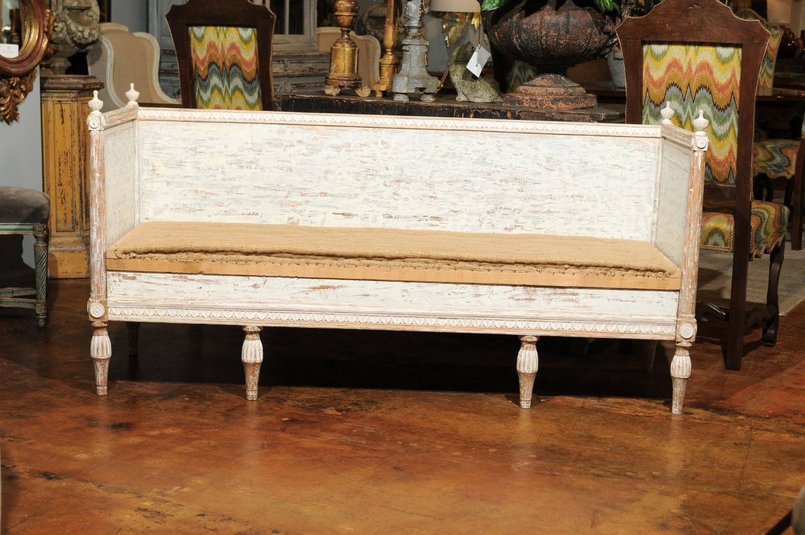 An Italian Neoclassical style painted and hand carved wooden bench from the mid-19th century, with distressed finish, under storage, finials, medallions and burlap upholstery. Born in Italy during the mid-19th century, this exquisite wooden bench