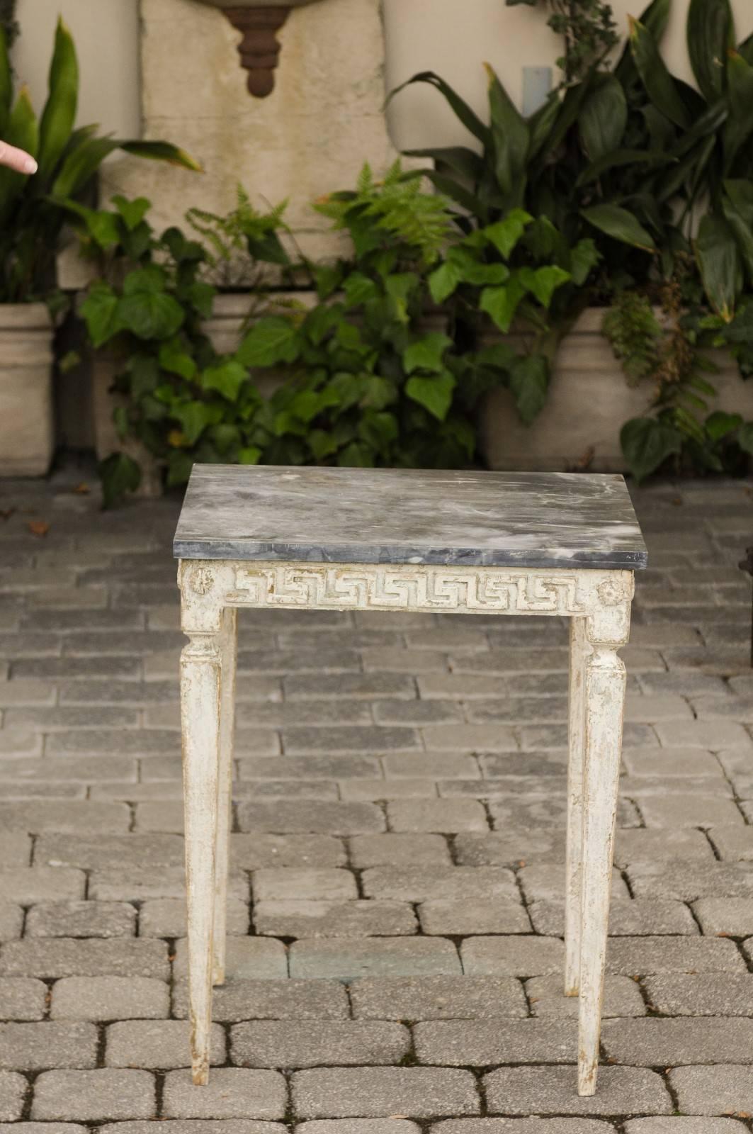 An Italian neoclassical style painted wood side table from the early 20th century, with veined marble top and Greek key frieze. This Italian neoclassical table features a rectangular dark veined marble top sitting above an exquisite apron carved