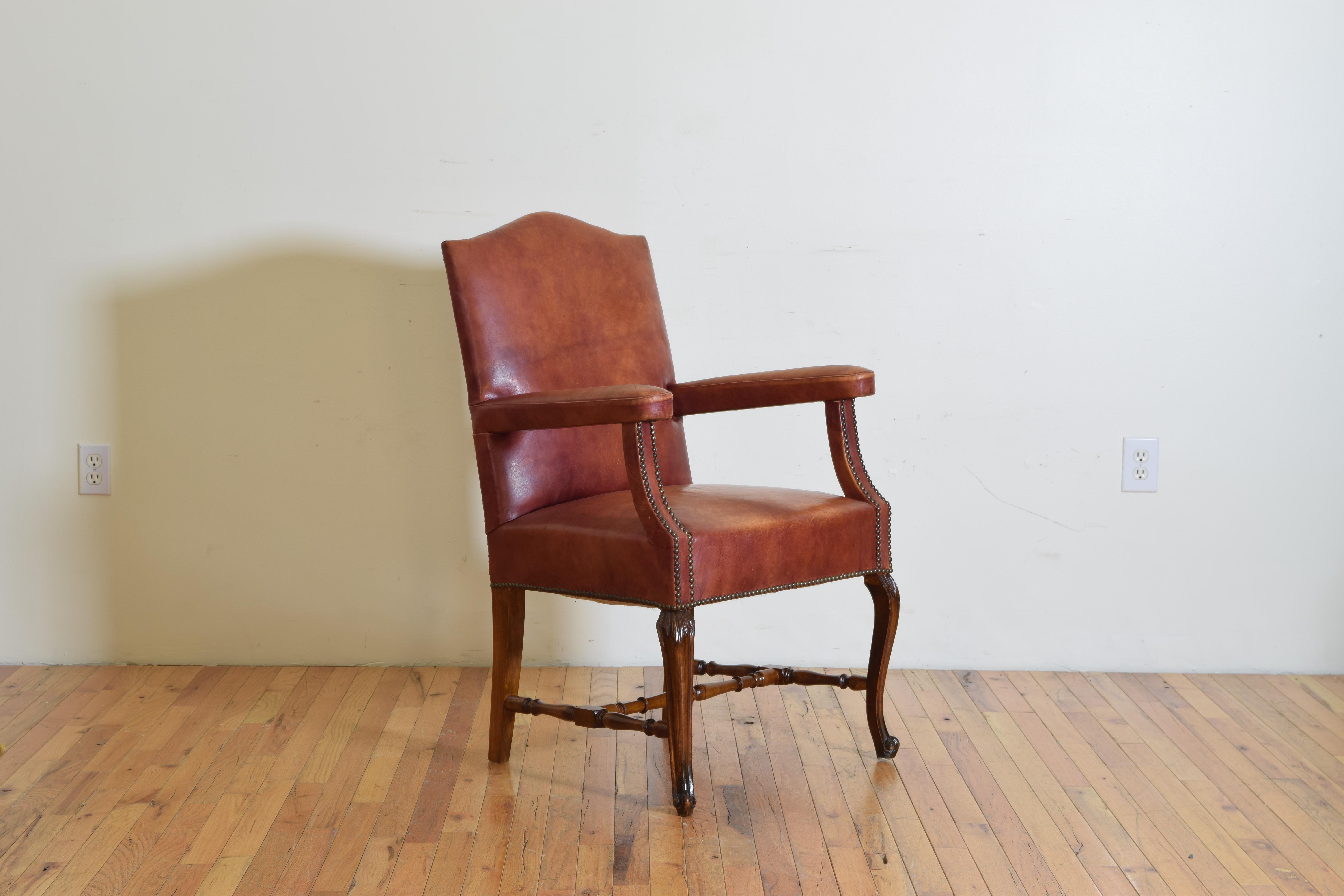 Having an arched backrest, upholstered arms, the walnut frame with slight cabriole legs joined by a turned stretcher, 1st half of the 20th century.