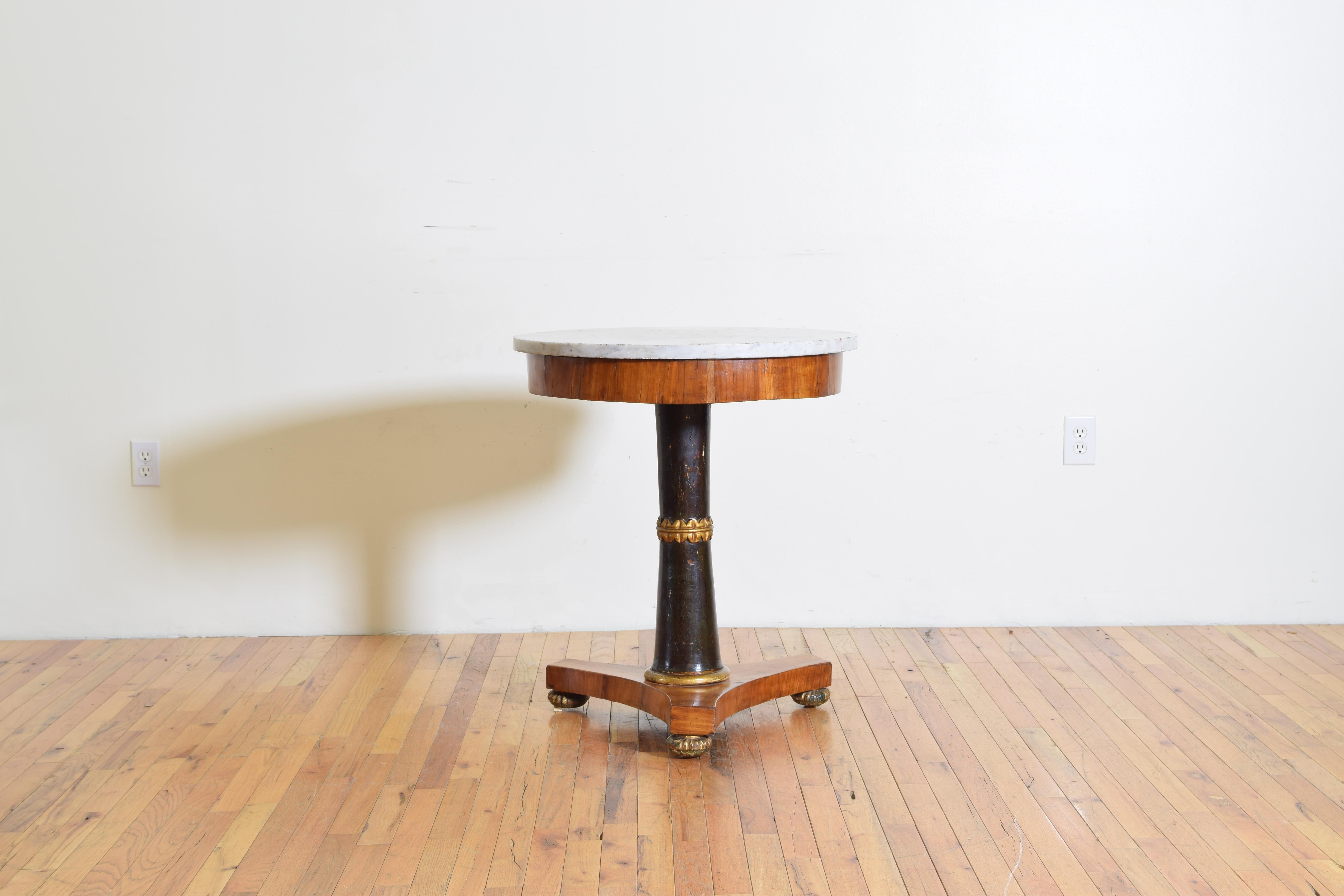 The original marble top above a conforming apron covered in walnut veneer supported by and ebonized columnar standard divided by a carved giltwood decoration, the tripartite walnut veneered base raised on carved and gilded bun feet, circa 1825.