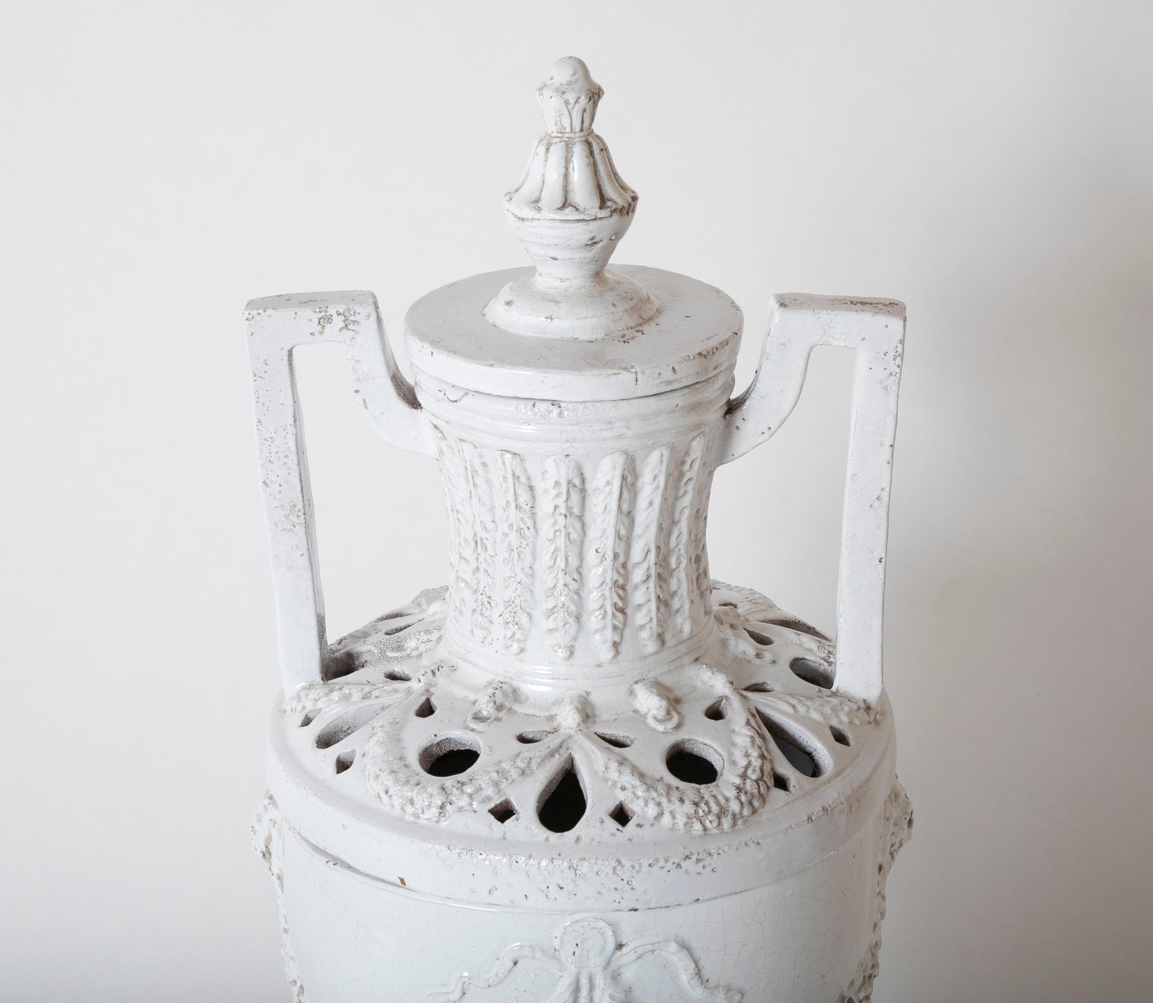 Urna in ceramica smaltata bianca in stile neoclassico italiano. Questo classico vaso toscano è un raffinato complemento decorativo per interni tradizionali e contemporanei. Realizzato a mano in ceramica e smaltato di bianco, presenta una silhouette