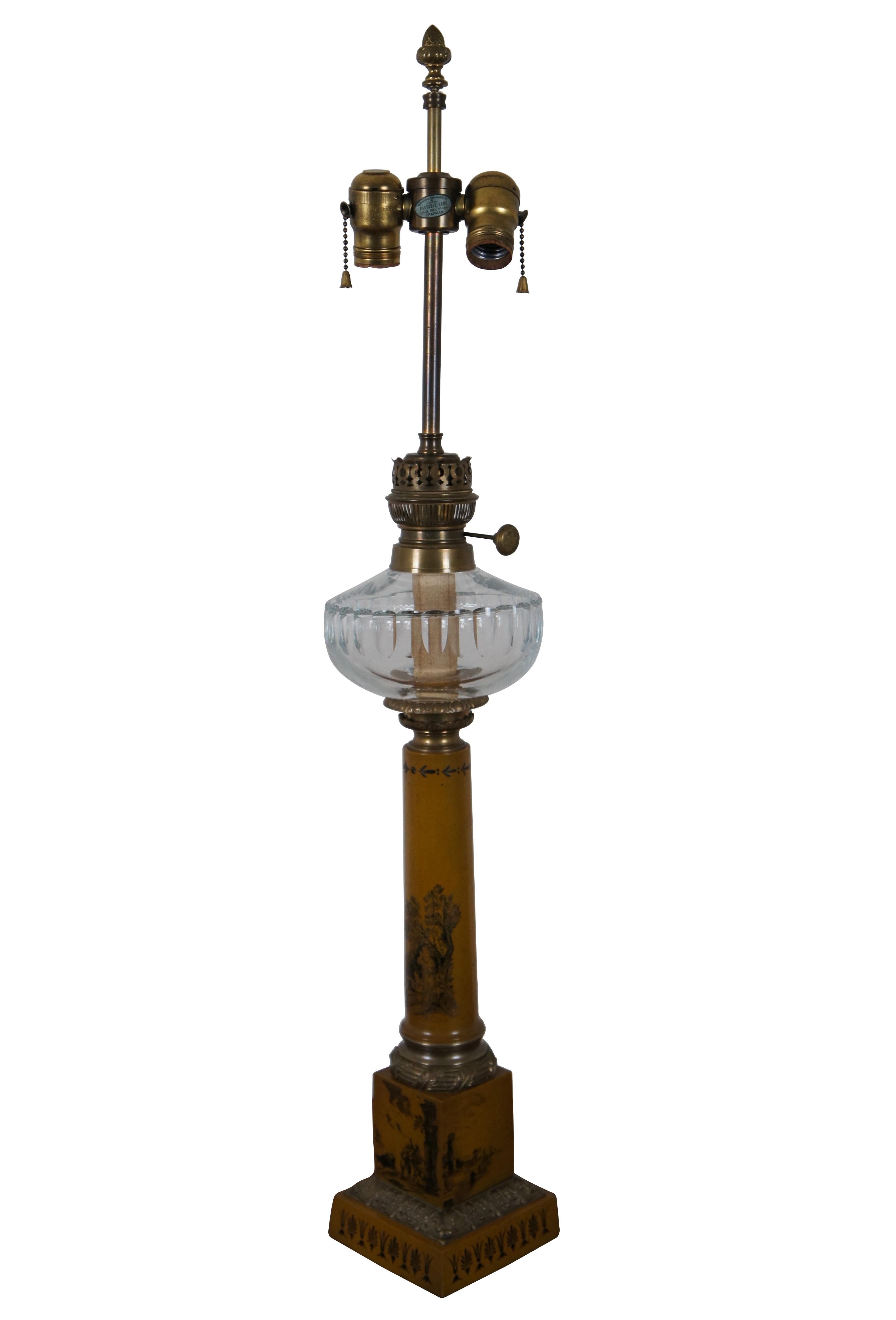 Vintage 20th century converted oil table lamp in the shape of a Italian Neoclassical tole column painted in mustard yellow with toile Provincial scenes / landscapes, trimmed in brass and topped with a clear glass reservoir below the two light