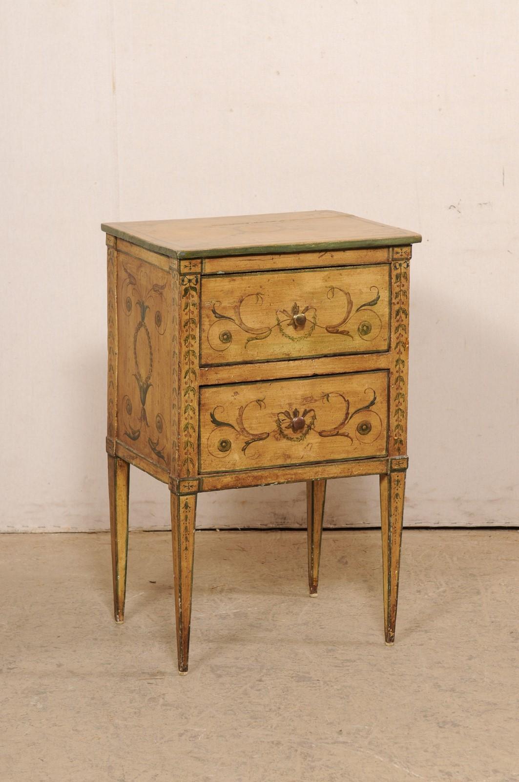 An Italian raised two-drawer painted wood side chest from the 19th century. This antique petite sized chest from Italy is comprised of clean/straight lines, which has been nicely complimented with beautiful hand-painted foliate of wispy leaves and