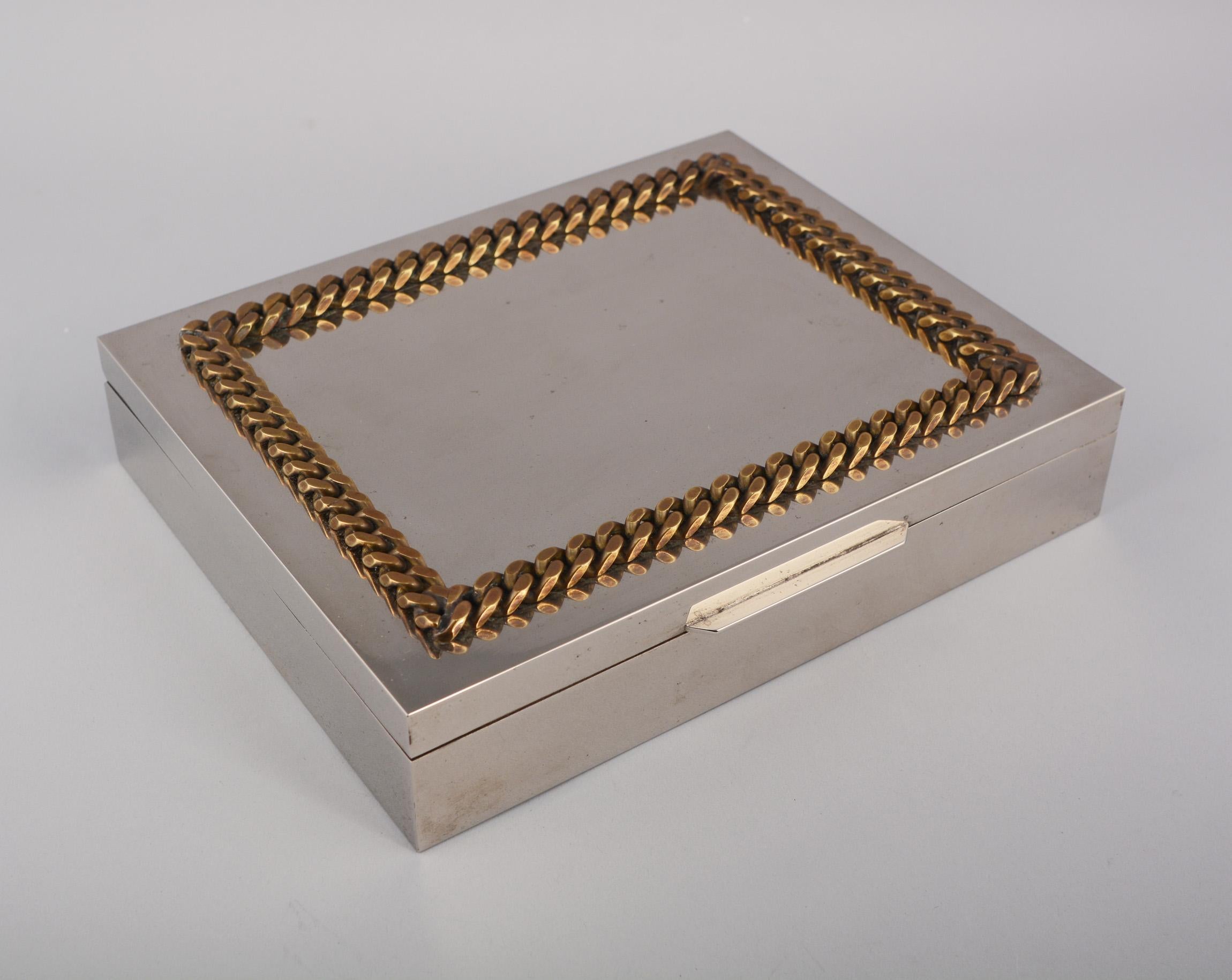 Nickel plate cigar or trinket box with satinwood lined interior. This has a heavy brass chain around the top of the lid. The box retains a made in Italy label on the bottom. The interior compartments are 6 7/8 inches by 4 3/8 inches. This has a few