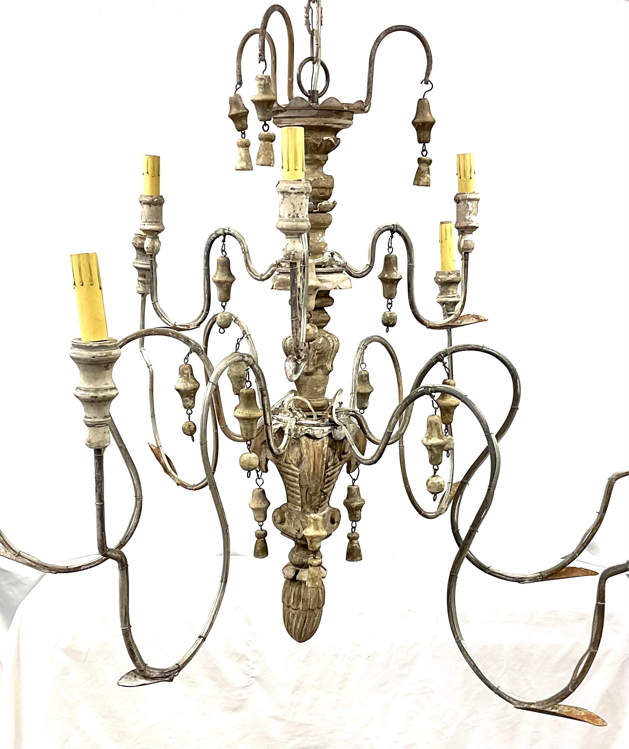 An Italian nine arm chandelier comprised of antique elements. Aged patina and neutral colors. Scrolling wrought iron arms with carved and turned grey painted wood baluster, gilt wood tassel and bell hanging decoration, all now with a wonderful aged