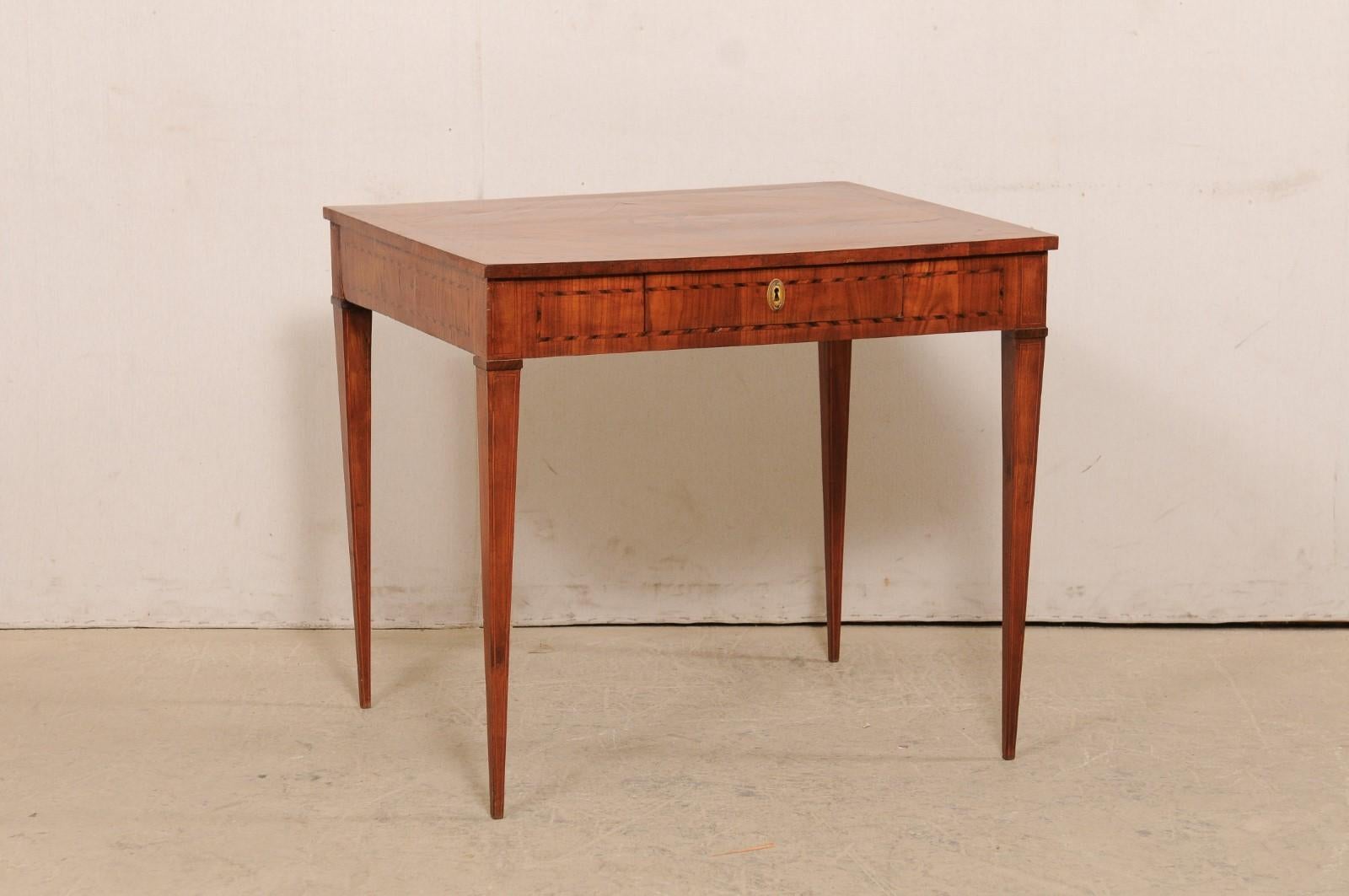 An Italian occasional table or small writing desk from the early 19th century. This antique table from Italy is beautifully decorated with a fanned medallion inlay featured prominently at it's top center, and a ribbon banding inlay outlines the top