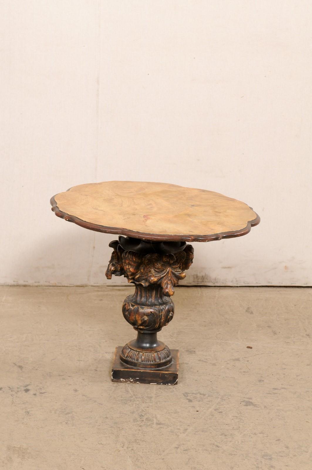 An Italian side table, with putto and urn carved pedestal base, from the 19th century. This antique table from Italy features a round-shaped top with faux-marble finish and scalloped edges, above an urn, putto, and foliate carved pedestal, and