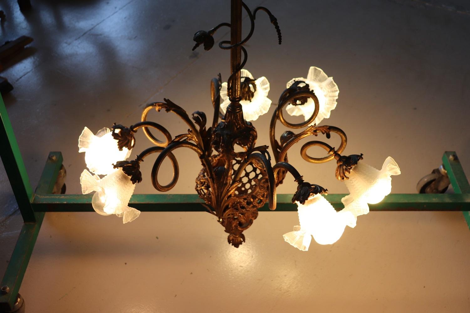 Beautiful and refined Italian 1910s of the period Art Nouveau chandelier with 6 bulbs. The lights are arranged on different floors. In gilded chiseled bronze completely. The six arms are in the shape of a flower and end in a glass shade. Chandelier