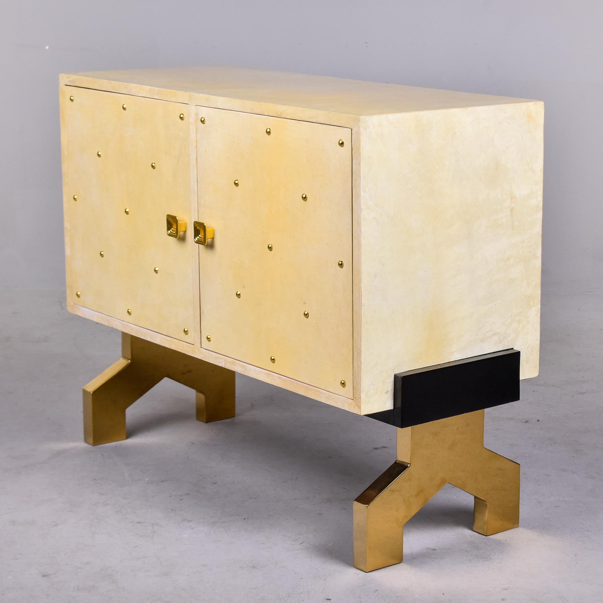 Circa 1980s Italian two door cabinet is covered in off-white parchment and accented with brass studs. Chaque porte à charnière s'ouvre sur un espace de rangement avec une seule étagère intérieure. Les portes sont dotées d'une quincaillerie en