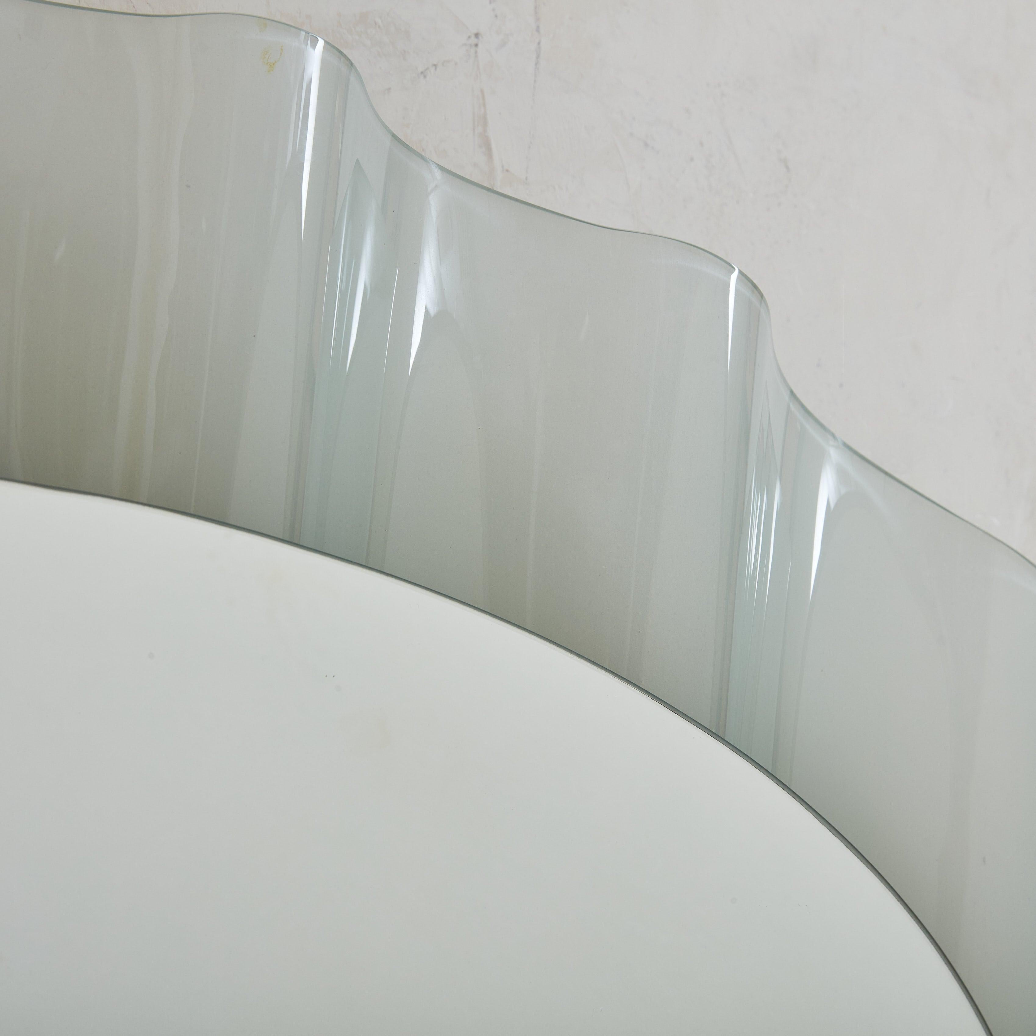 A rare Italian ‘Onda’ wall mirror designed by Nanda Vigo for Glas Italia in the 1980s. The oval mirror glass gracefully rests upon a satin glass frame, rendered in a muted aqua hue that features delicate ripples. The wavy outer edge introduces a
