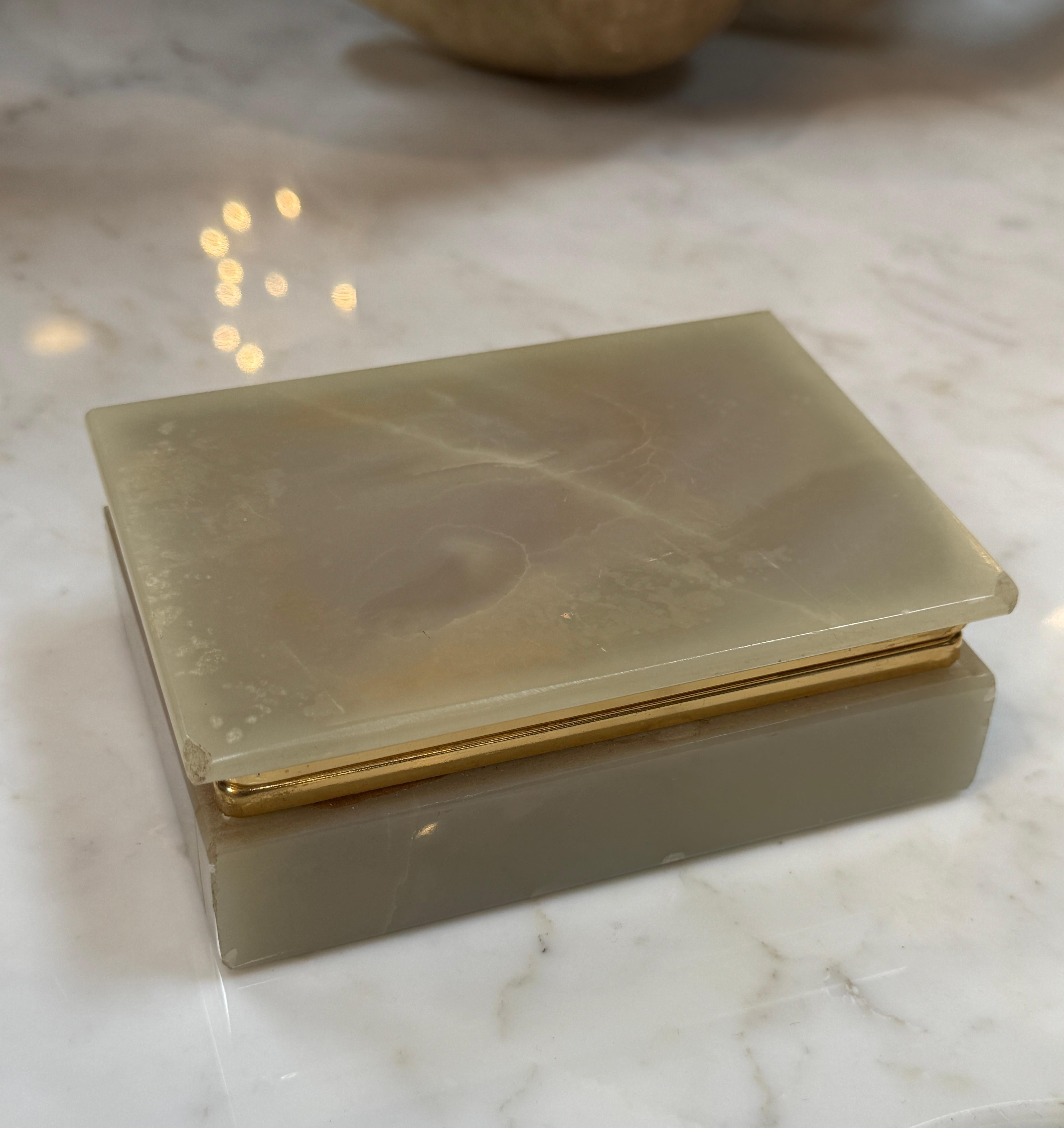 Cette boîte à bijoux vintage, fabriquée en onyx lisse et poli, respire l'élégance intemporelle. La pierre naturelle présente des veines délicates et terreuses, complétées par une garniture en laiton raffinée qui ajoute une touche de sophistication.