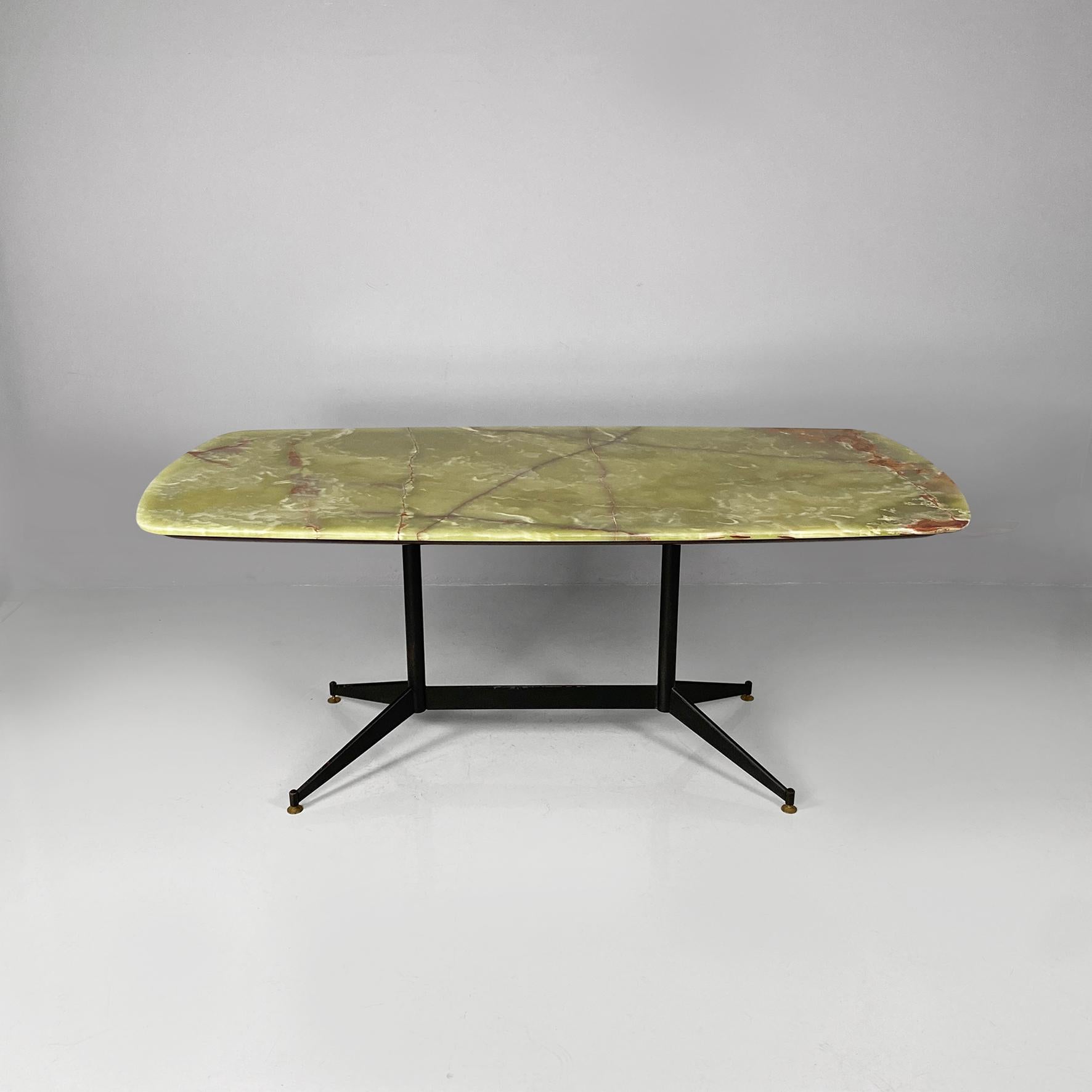 Tavolo da pranzo in marmo onice e metallo con forma rettangolare e angoli arrotondati. Basamento in metallo nero con quattro gambe in metallo e punte in ottone. Piano in onice dalle curve morbide e di grande peso e spessore, con le sue classiche