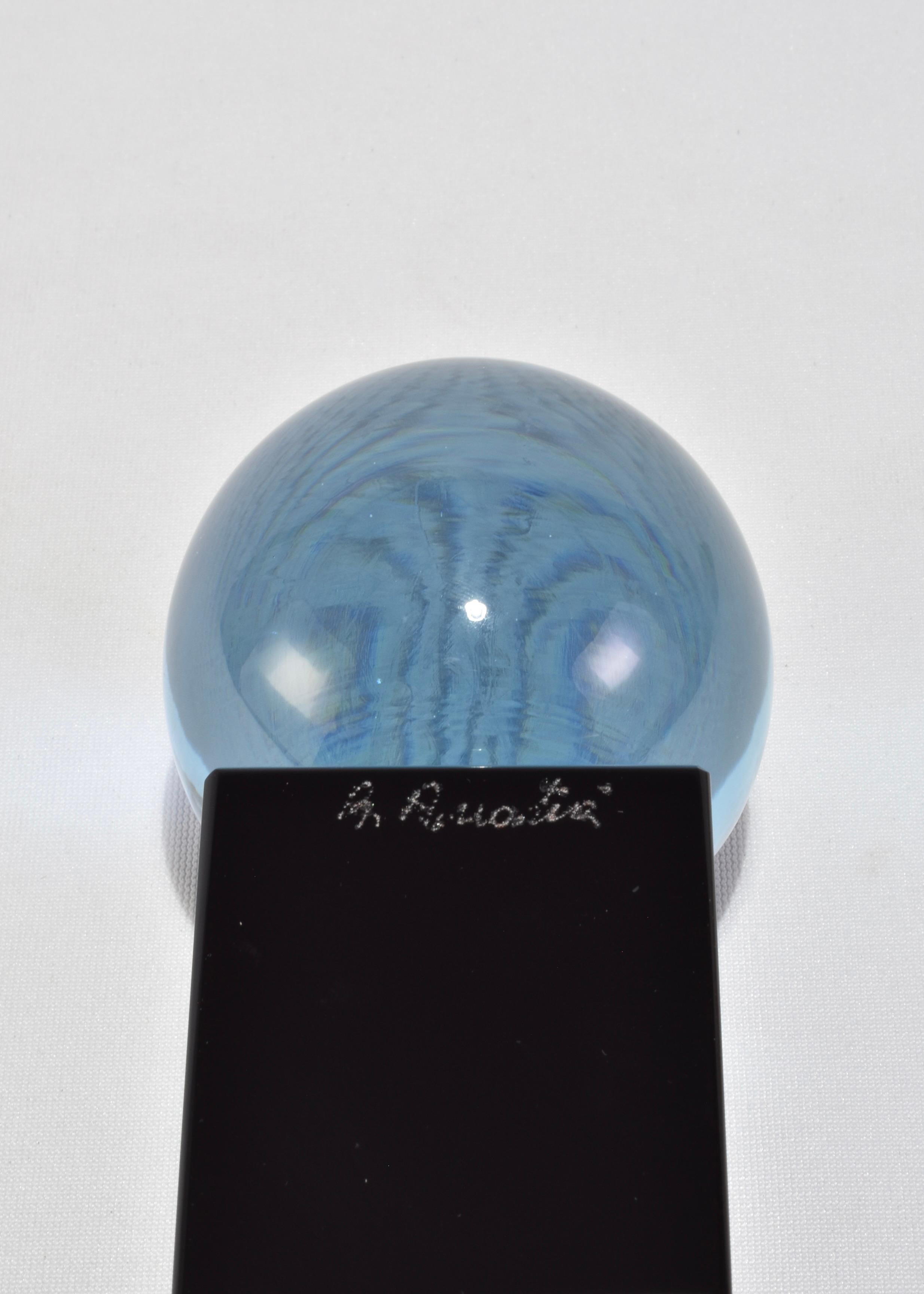 Striking optical glass sphere in a smoky blue hue, mounted on a black base. The sphere offers a lens-like visual effect, distorting and reflecting its surroundings with sculptural clarity.

Signed R. Anatra for renowned Murano glass artist Renato