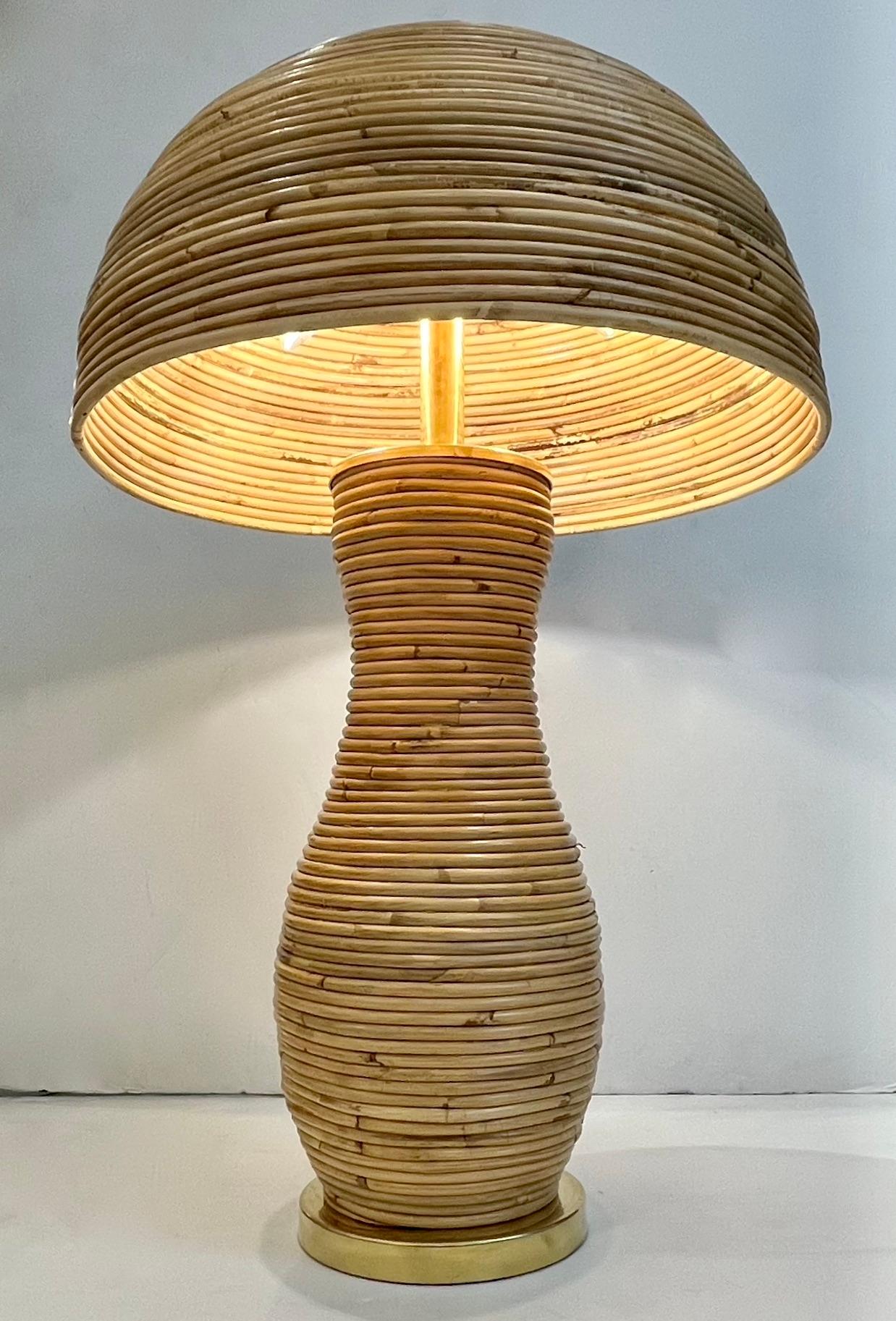 A contemporary organic modern creation, entirely handcrafted in Italy, a mushroom bamboo table lamp, the sensuous curved body entirely decorated in rattan on a brass round base and fitted with an elegant half moon shade also entirely in rattan